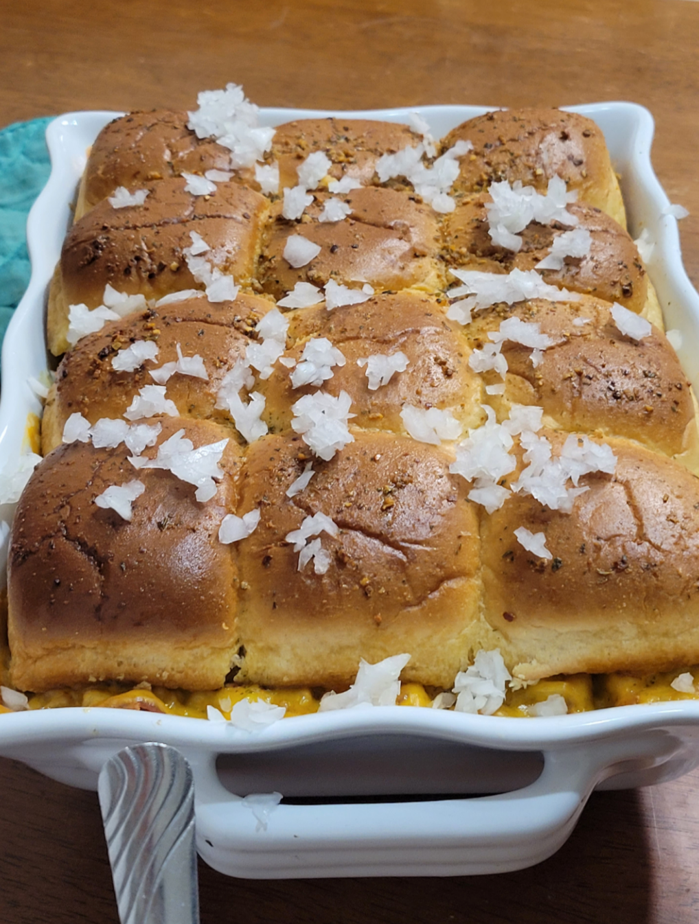 Baked slider buns with melted cheese and sprinkled onions in a casserole dish, ready to be served