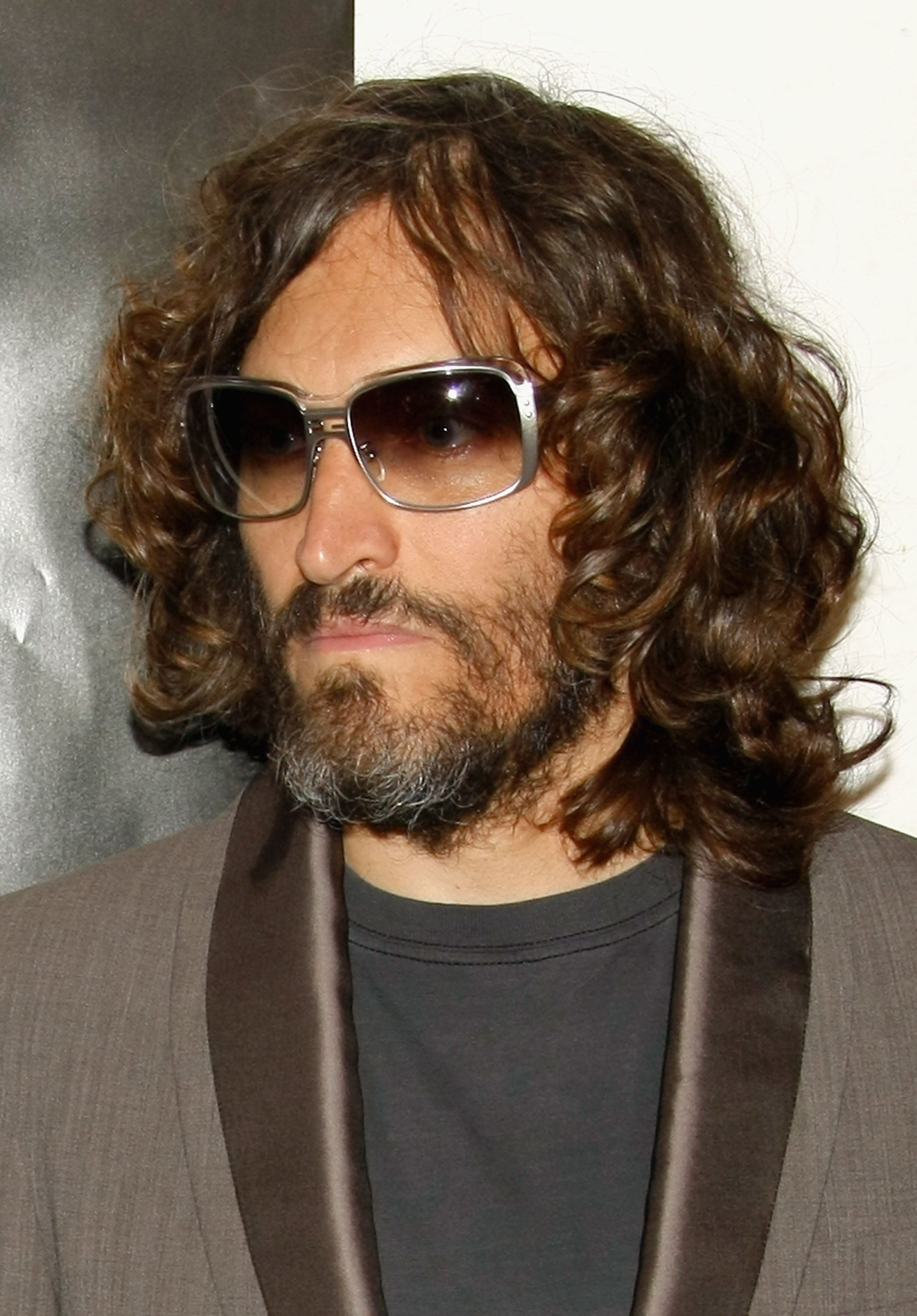 Vincent Gallo with curly hair and sunglasses in a blazer with satin lapels and a t-shirt, posing for a photograph
