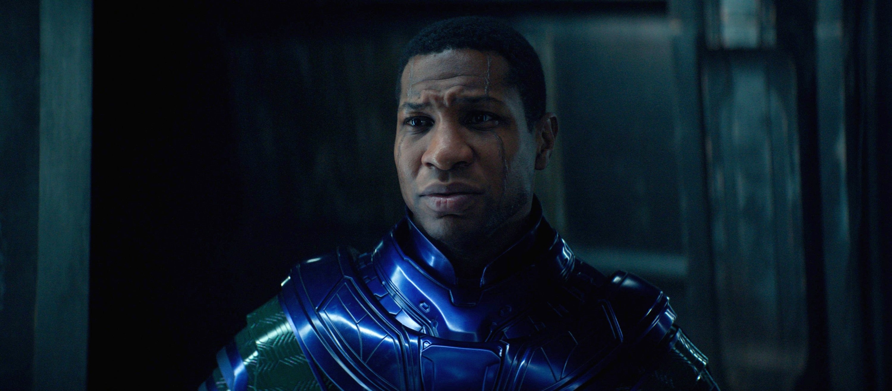 Jonathan Majors in a futuristic, metallic-style suit appears in a contemplative scene, set against a dimly lit background