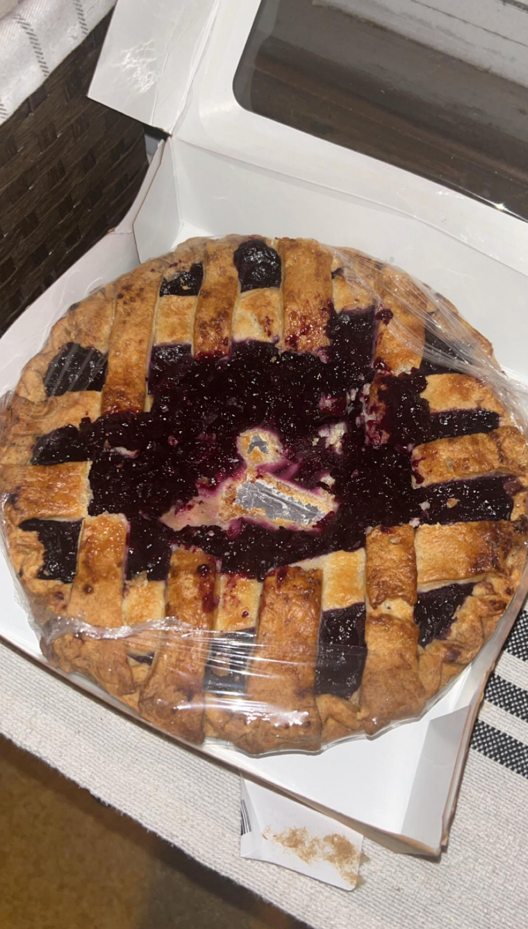 A lattice-topped fruit pie in an open box, partially wrapped in plastic