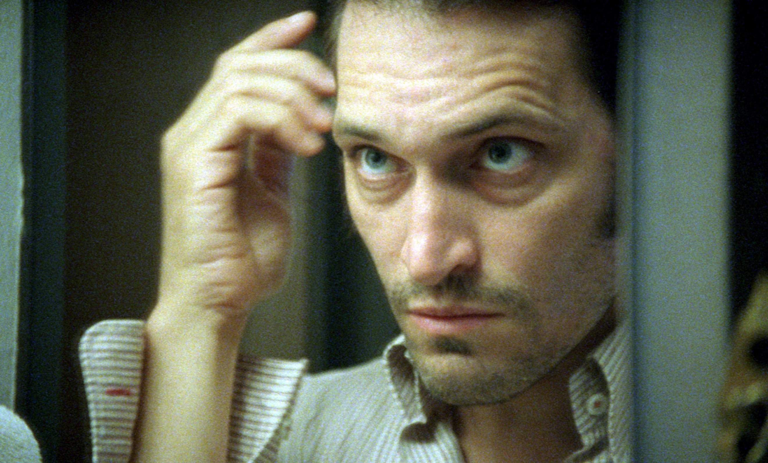 Vincent Gallo with a focused expression adjusts his hair, wearing a collared shirt indoors in a scene from The Brown Bunny