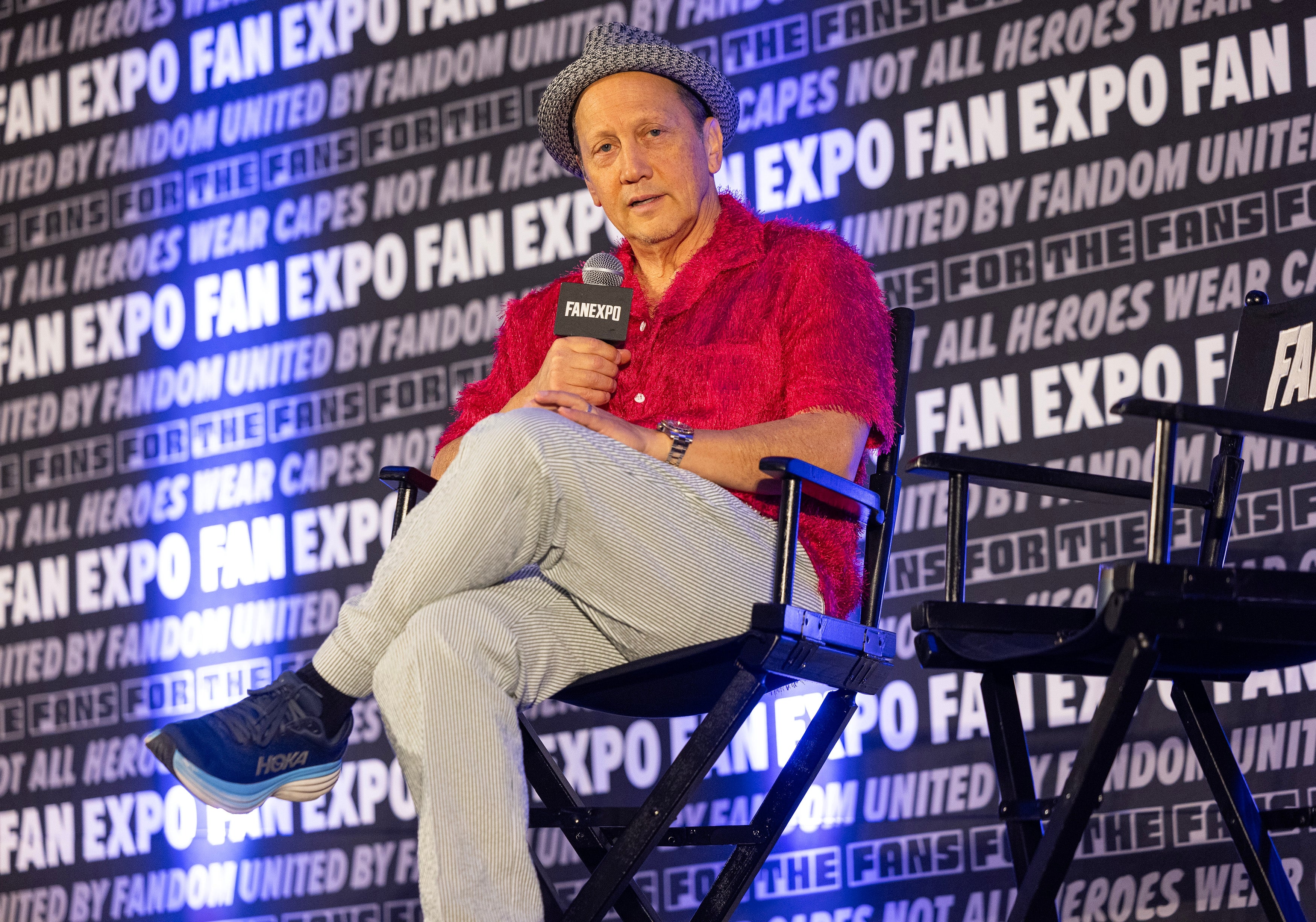 Rob Schneider in casual attire, seated on stage at Fan Expo, holding a microphone