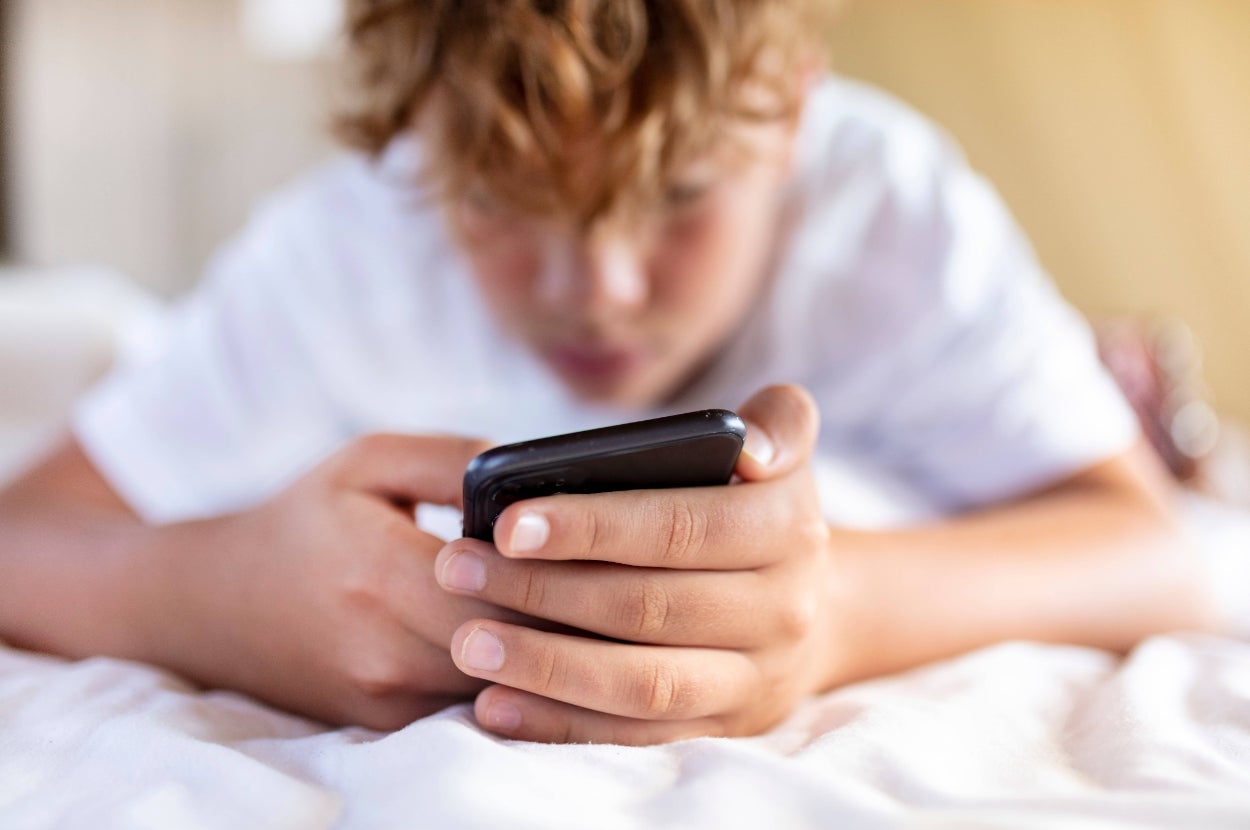 Child lying on bed, focused on using a smartphone