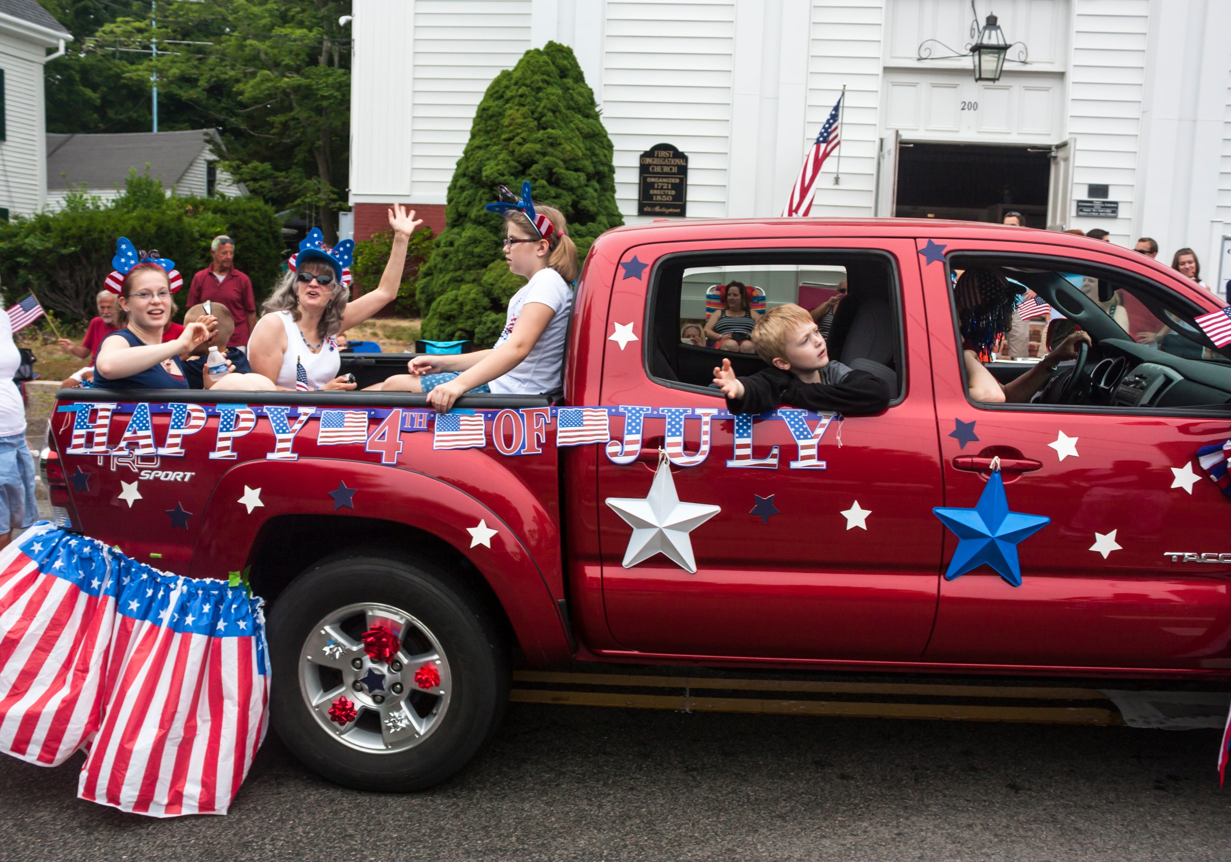 A motortruck decorated with "Happy 4th of July" banners, carrying radical with patriotic outfits, is portion of a festive parade