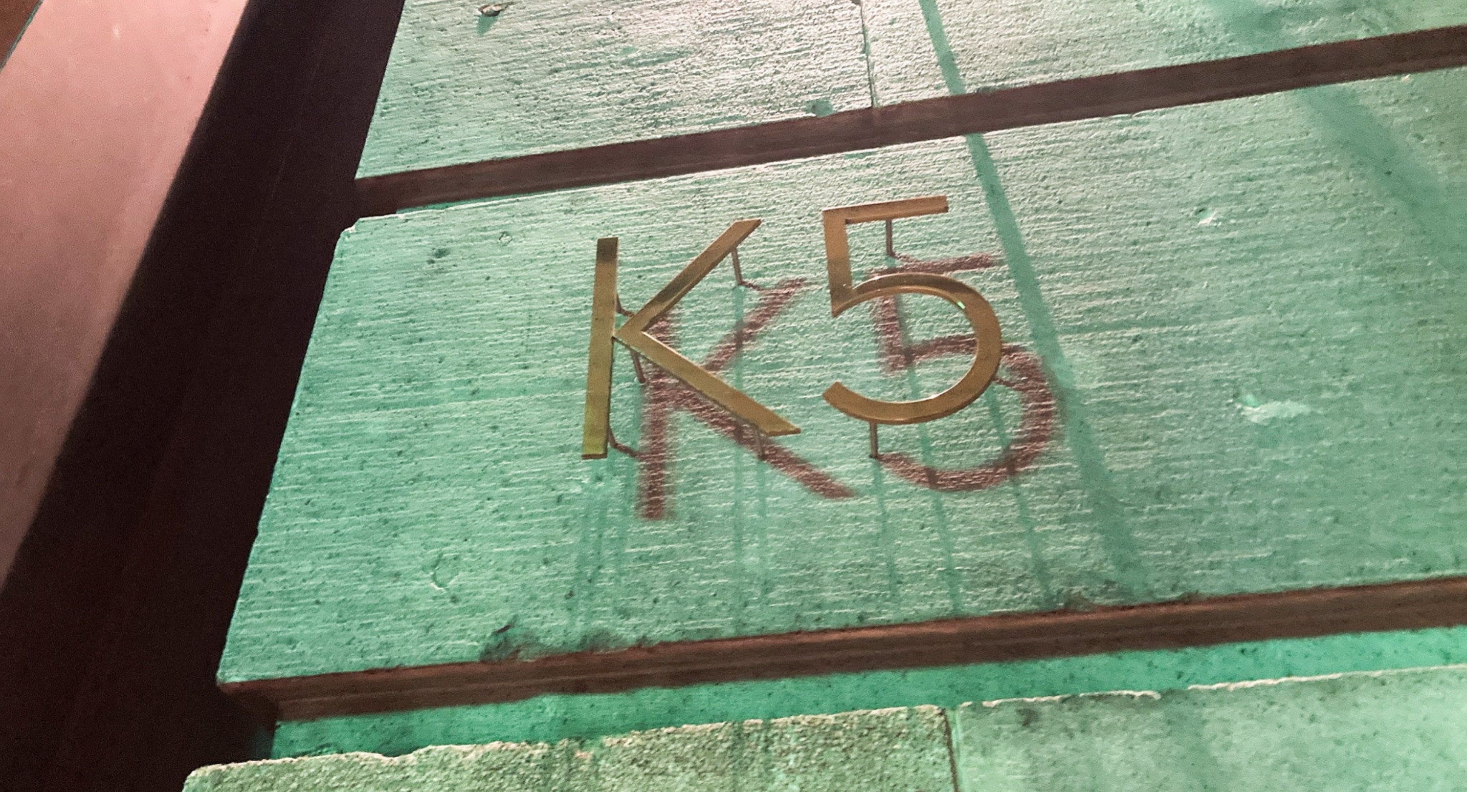 壁に「K5」と金色で書かれた看板。背景に消えかけた同じ文字が赤で描かれている。