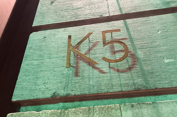 壁に「K5」と金色で書かれた看板。背景に消えかけた同じ文字が赤で描かれている。