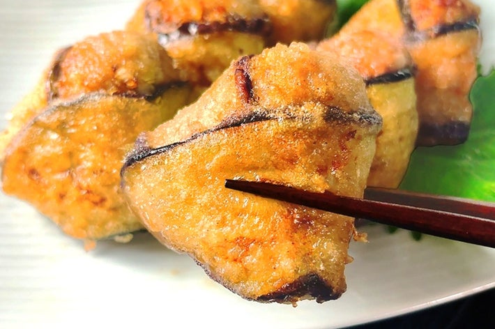 皿に盛り付けた餃子を箸でつかんでいる様子。美味しそうな焦げ目があり、青じその葉が添えられている。