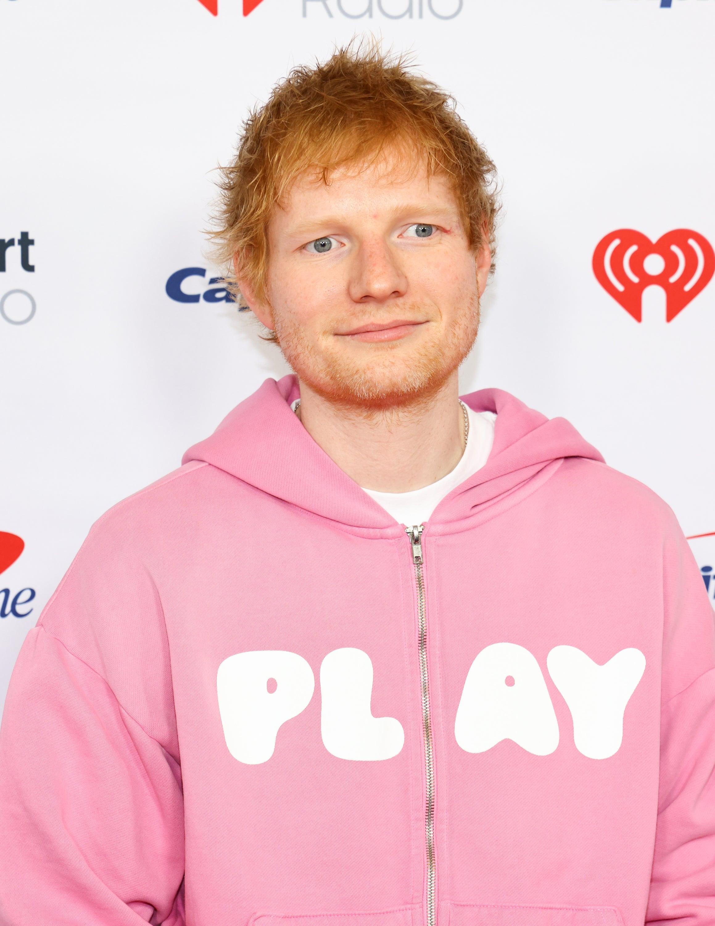 A person in a hoodie with the word "PLAY" stands in front of a backdrop with logos