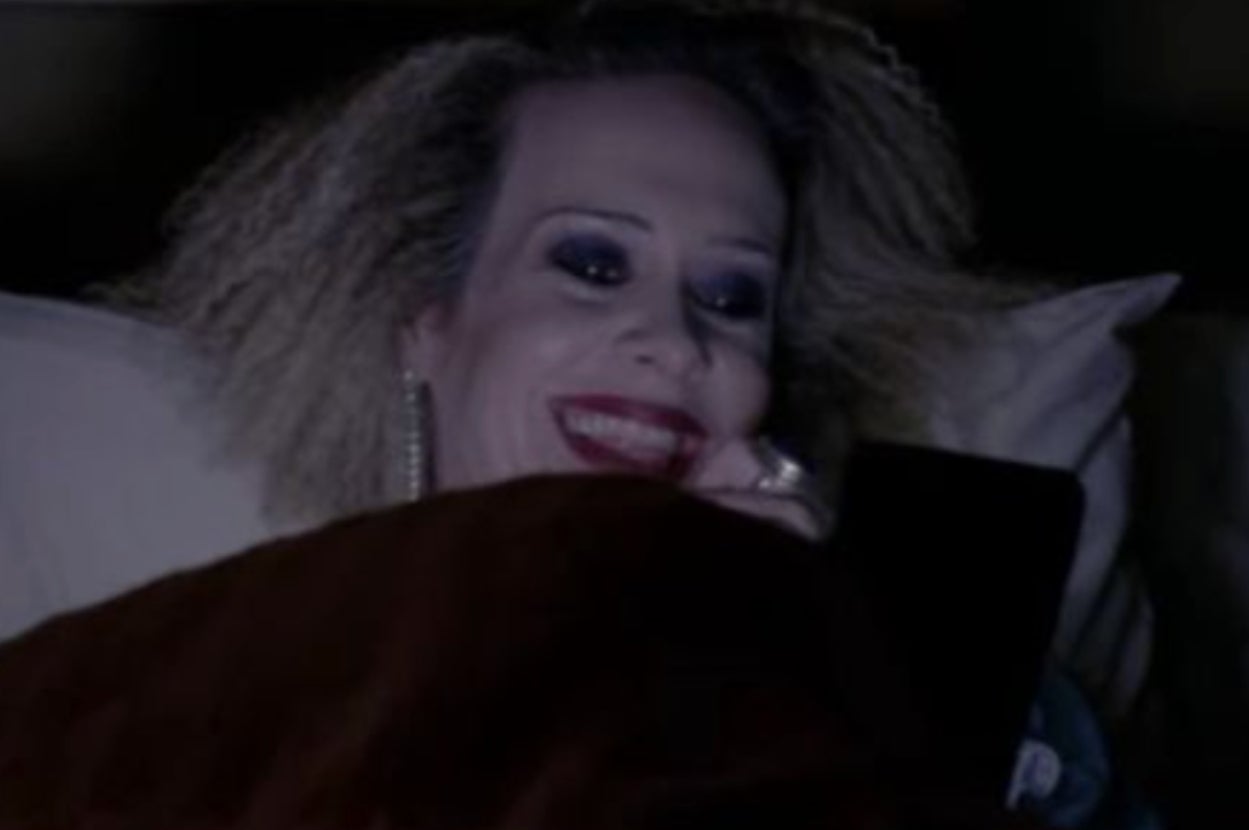 Person with voluminous hair lies in bed, smiling at a smartphone, appearing amused or entertained