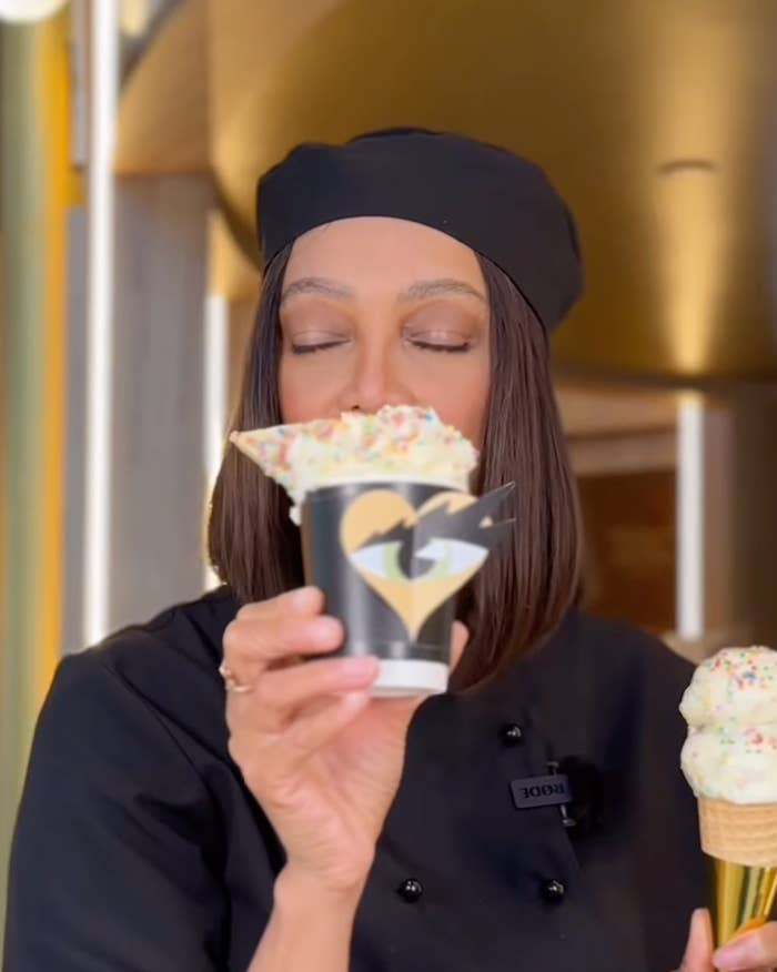 Tyra Banks in a chef's outfit holding an ice cream cone and cup, with eyes closed in delight