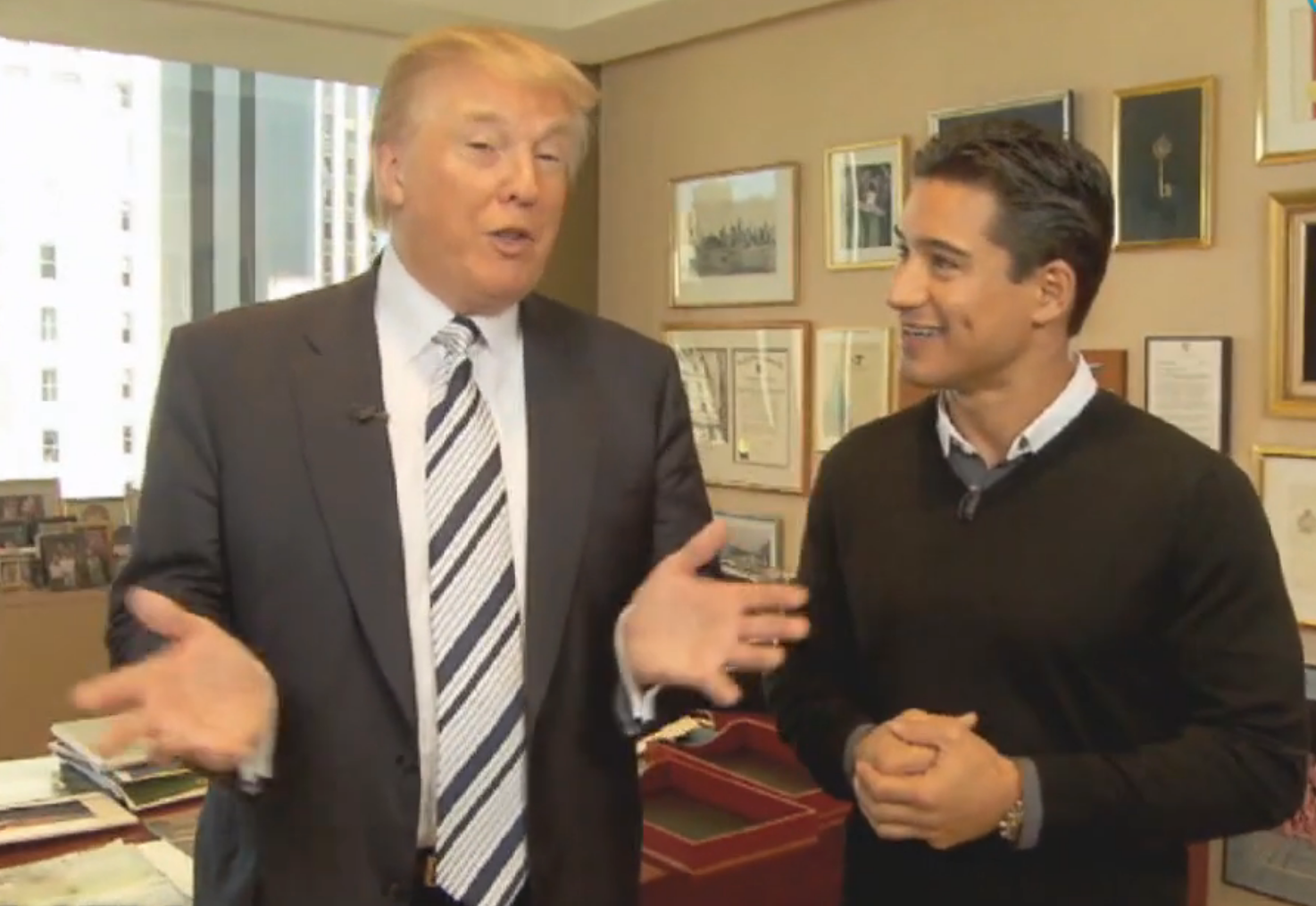Mario Lopez intervjuer Donald Trump i et kontormiljø med rammer hengende på en vegg i bakgrunnen