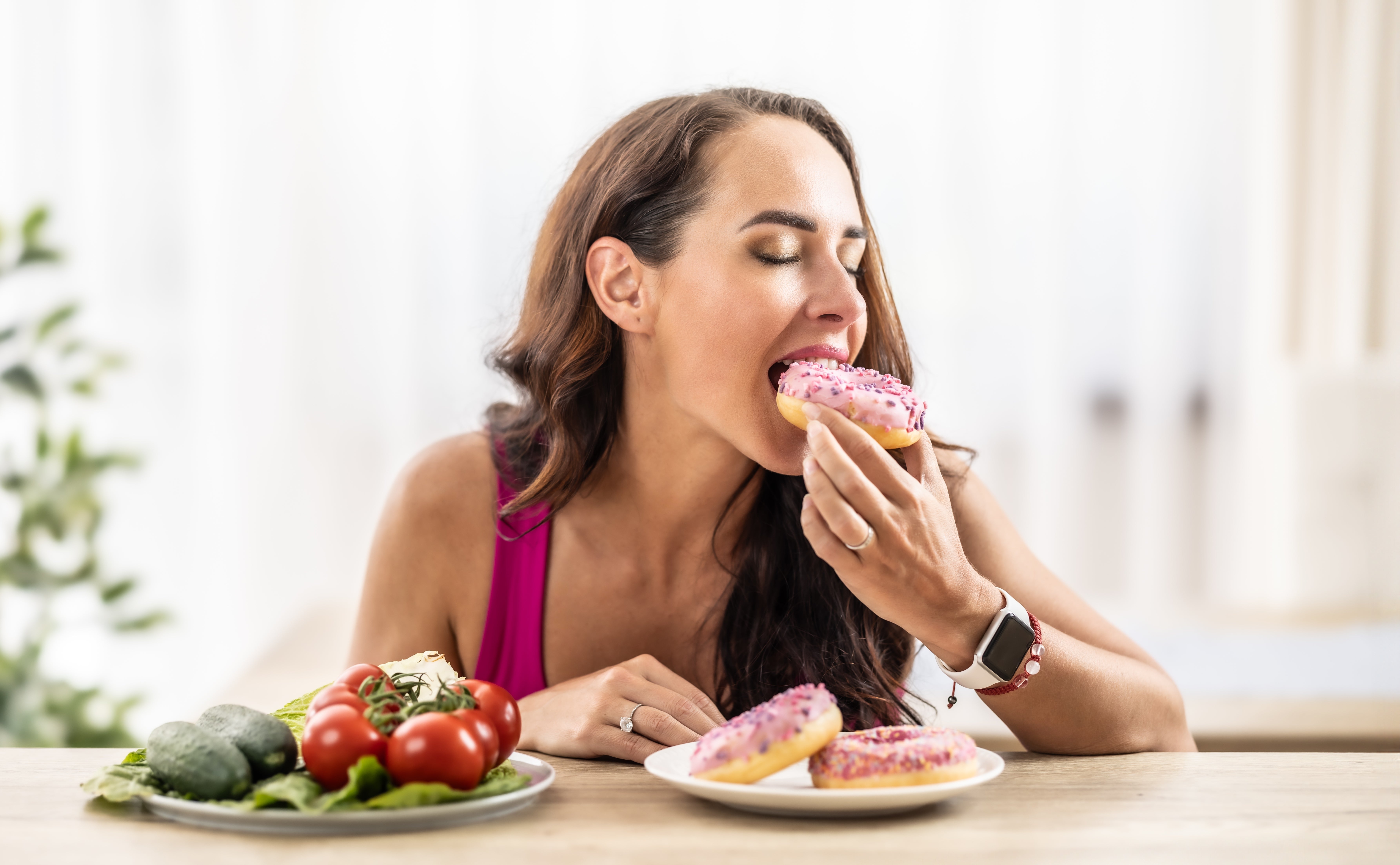 A pistillate   enjoys a pinkish  frosted donut with a sheet  of tomatoes and avocados nearby, illustrating a premix  of indulgence and steadfast   choices