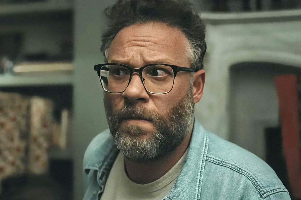 Man with glasses and beard looking concerned, indoors, wearing a denim shirt over a T-shirt