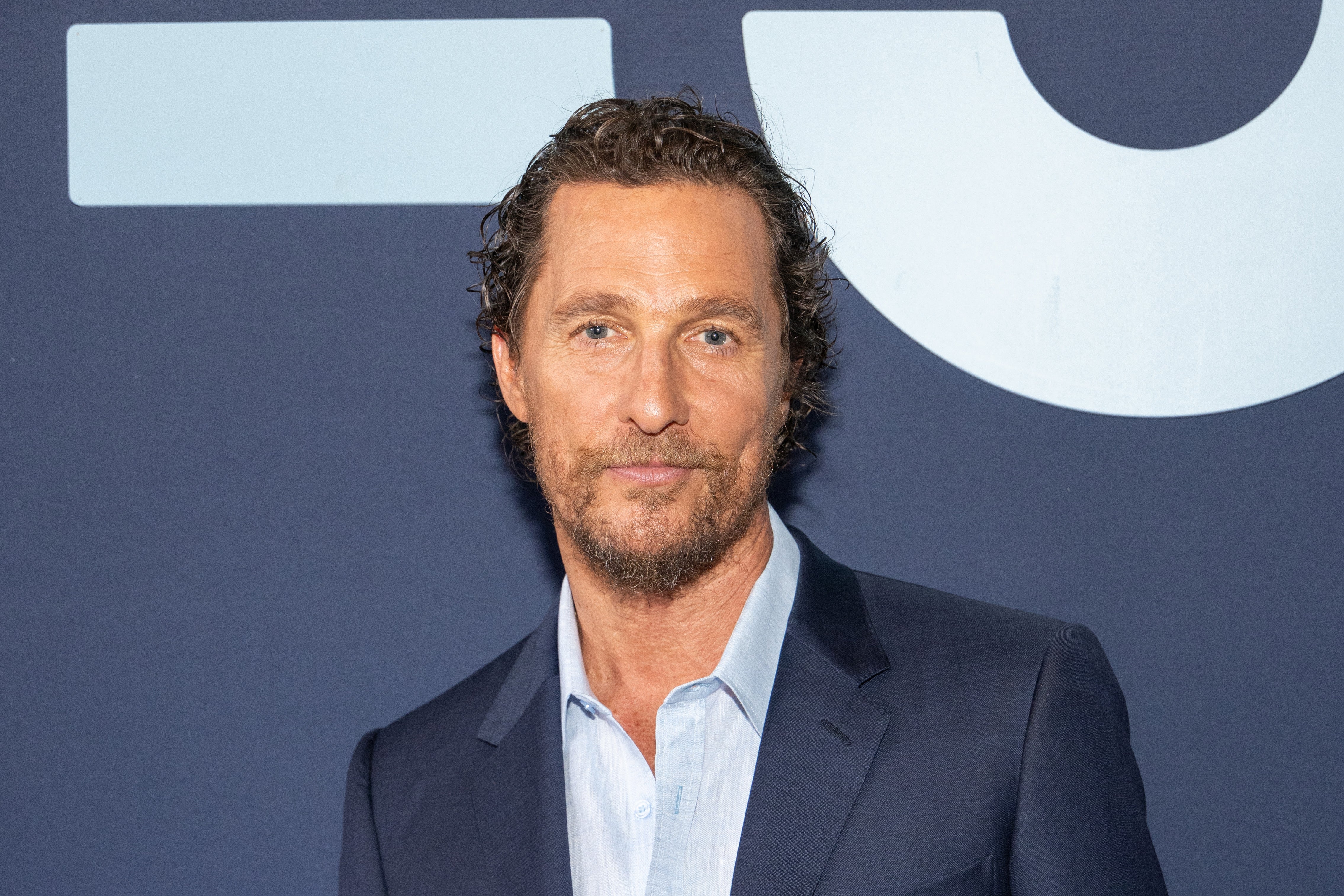 Matthew McConaughey in a suit stands on a stage backdrop