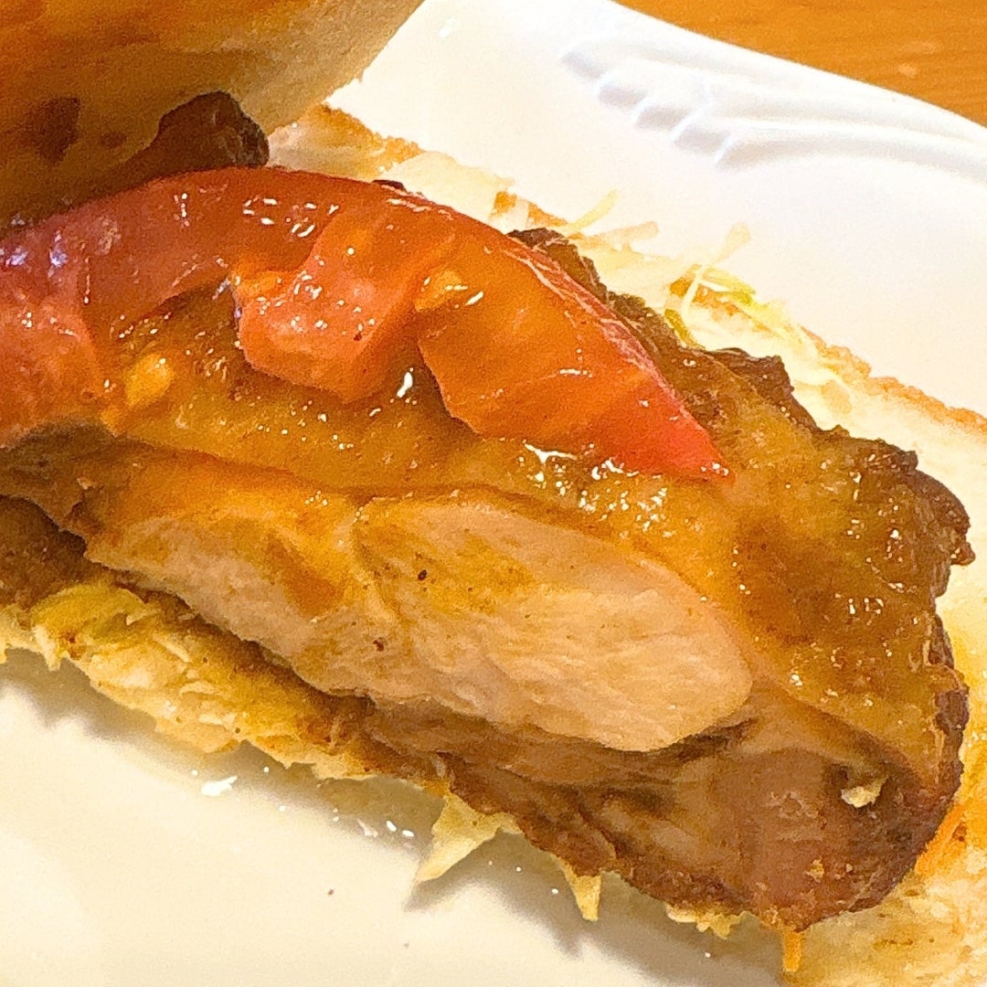 コメダ珈琲店の「タンドリーチキンホットサンド」のサンドイッチに挟まれたジューシーなチキンと赤いトマトをクローズアップ。