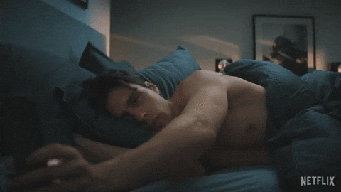Person lying in bed, reaching out sleepily. Bedroom with dim lighting in the background