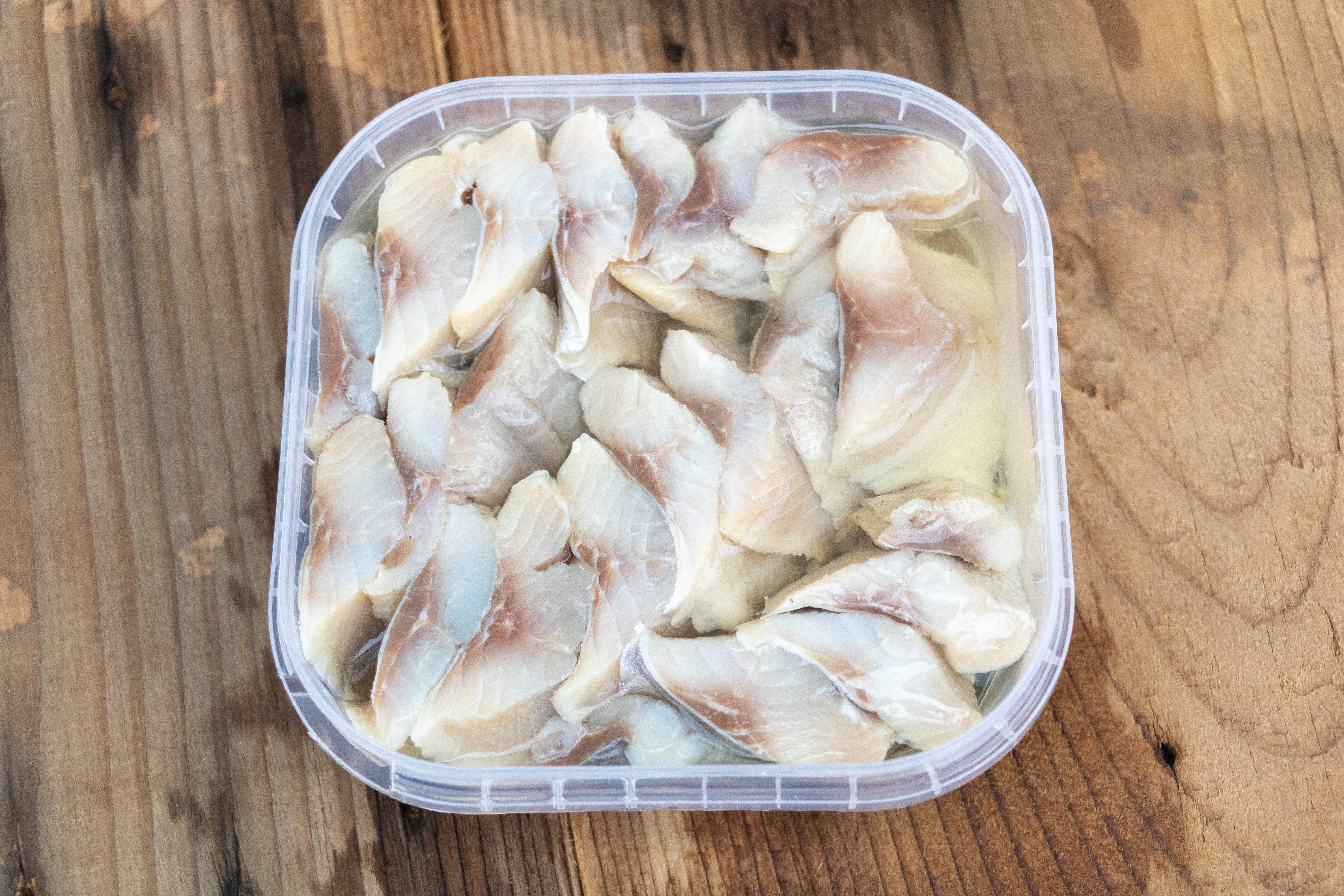 Plastic instrumentality filled with sliced, pickled herring connected a woody surface