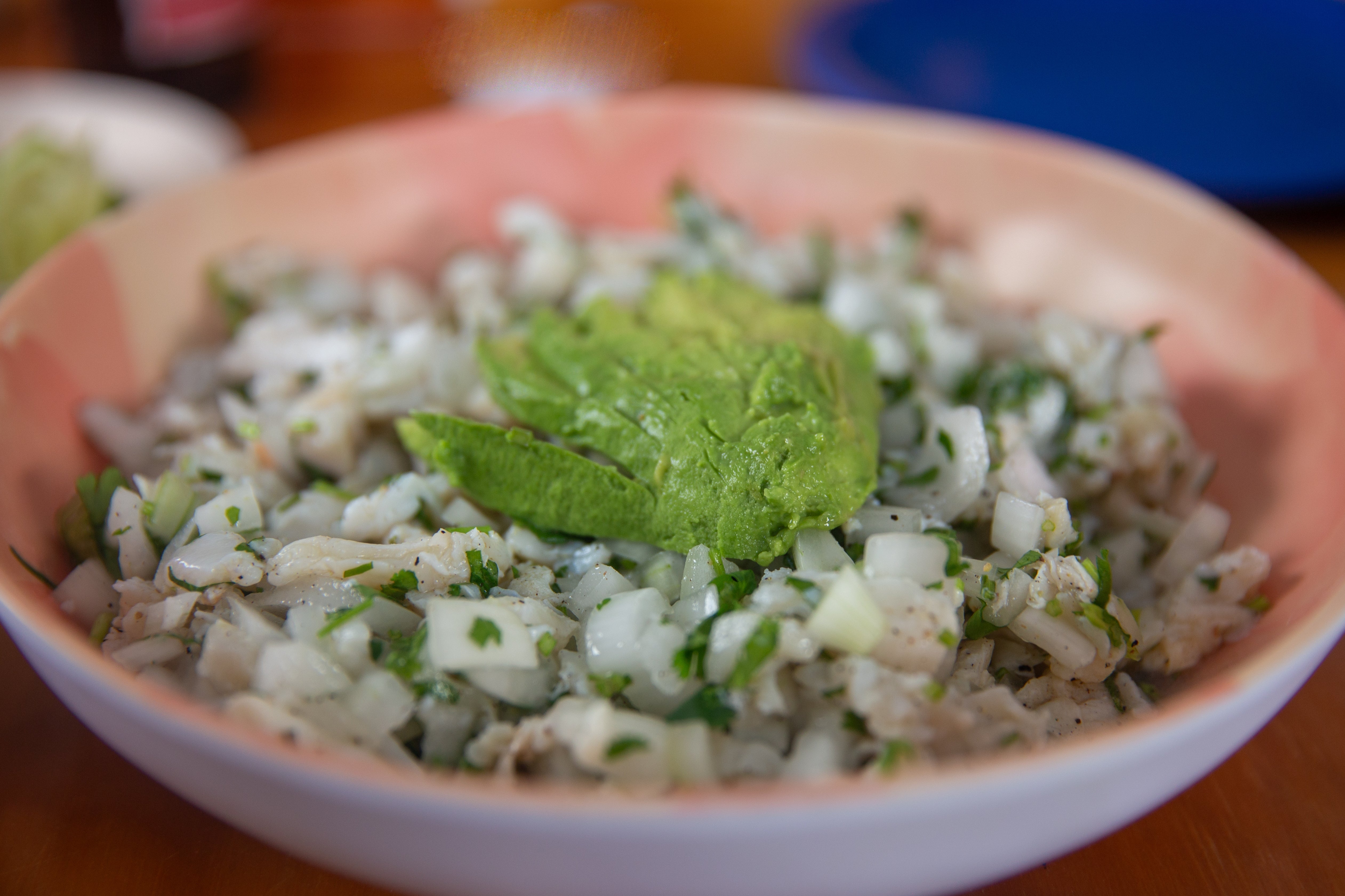 A vessel of ceviche topped with a portion of avocado, featuring diced food and herbs