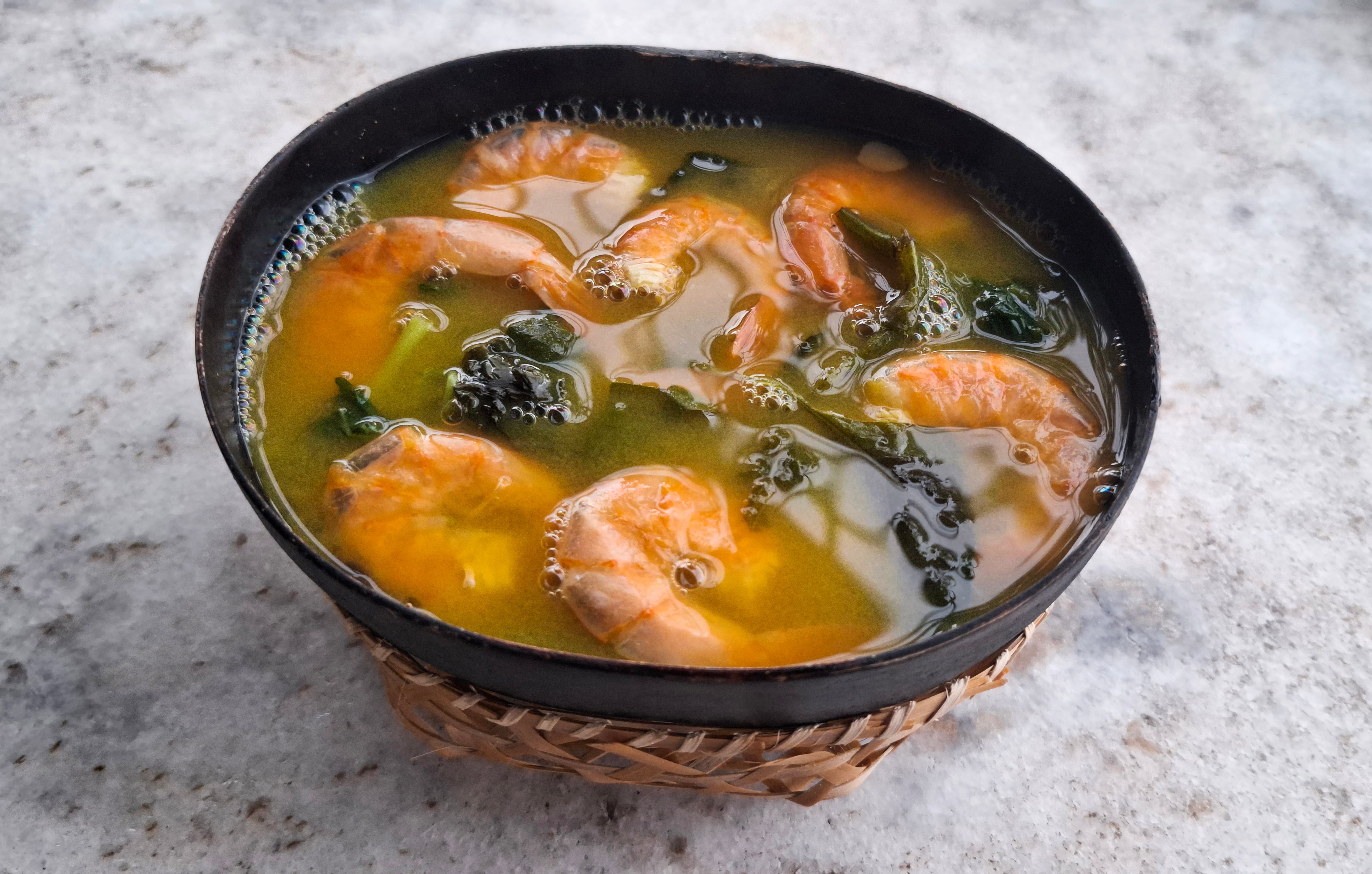 A vessel of shrimp crockery with greens, served successful a woven basket, connected a marble surface
