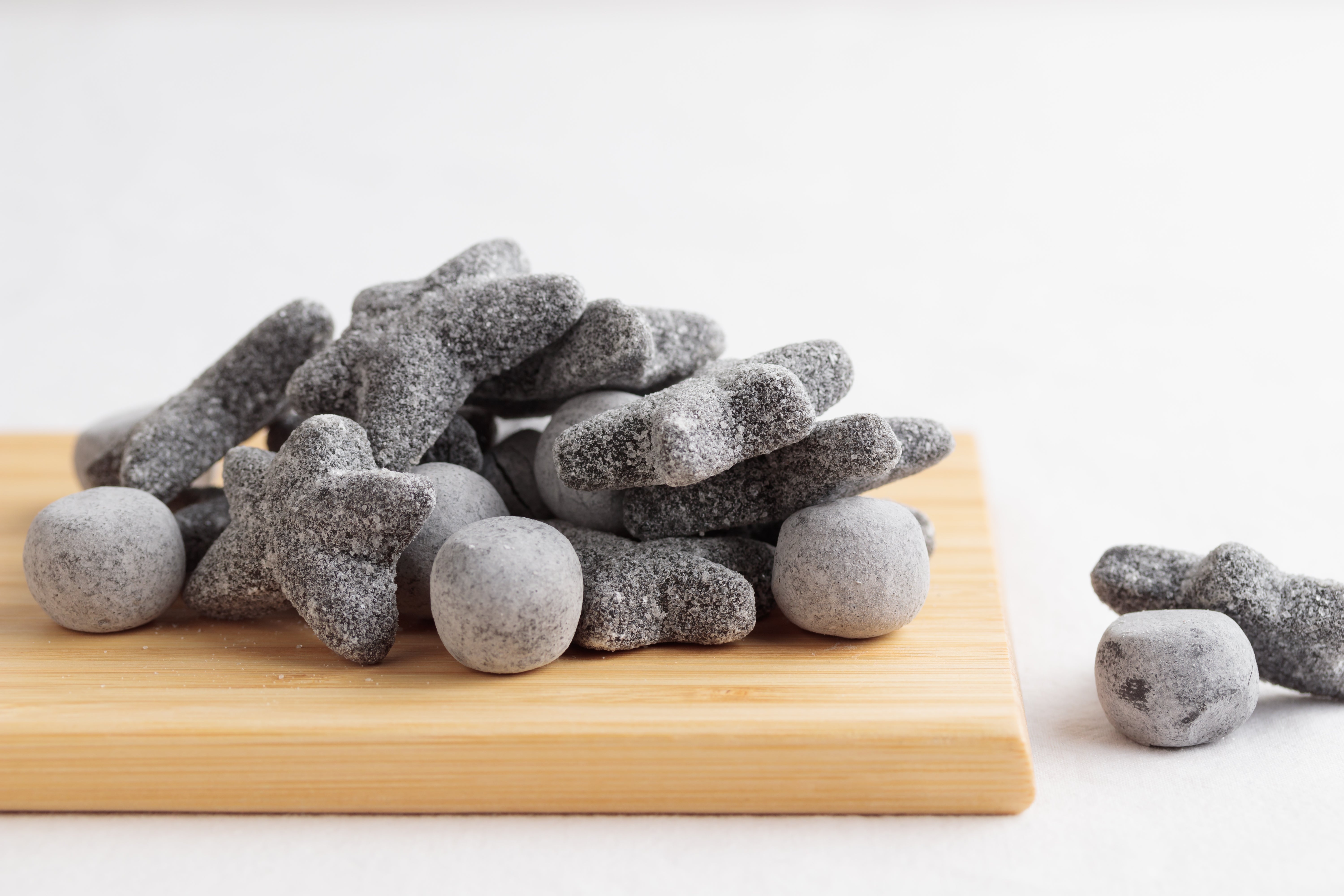 Pile of brackish licorice candies shaped similar stars and sticks connected a woody board, with a fewer pieces beside it
