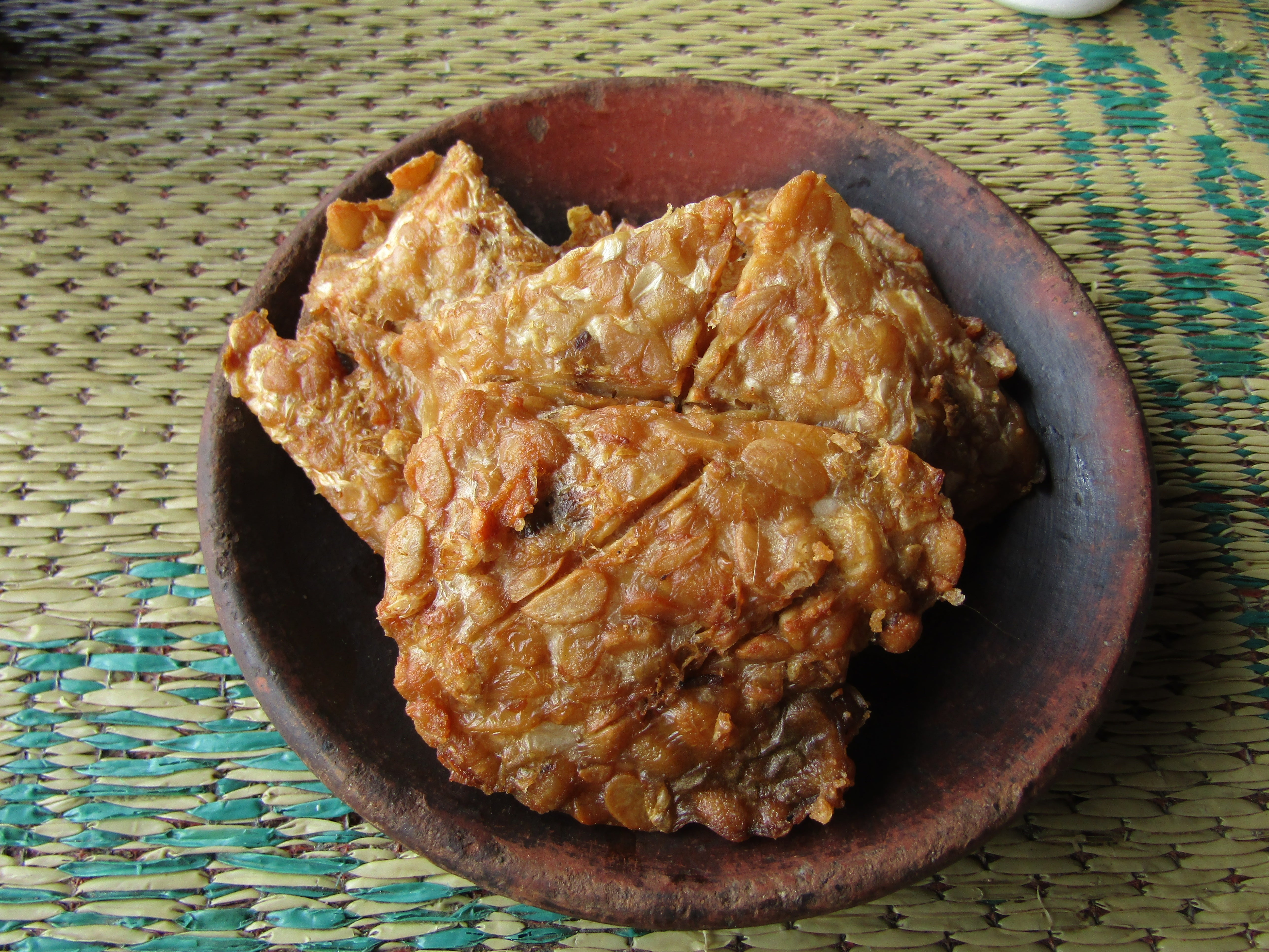 Fried tempeh slices connected a brownish sheet placed connected a woven mat
