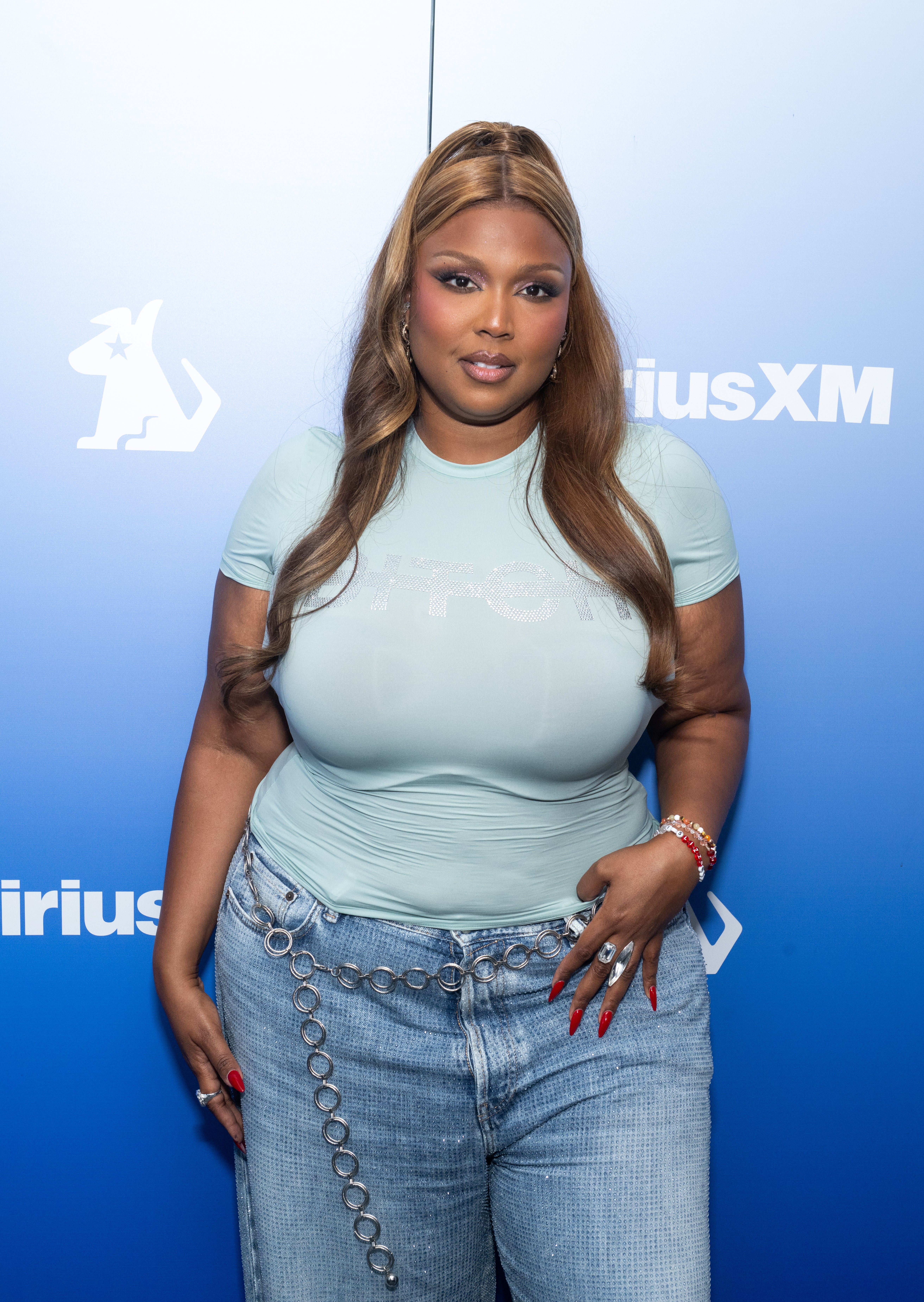 Lizzo wearing a fitted t-shirt and chain-embellished jeans poses at a SiriusXM event