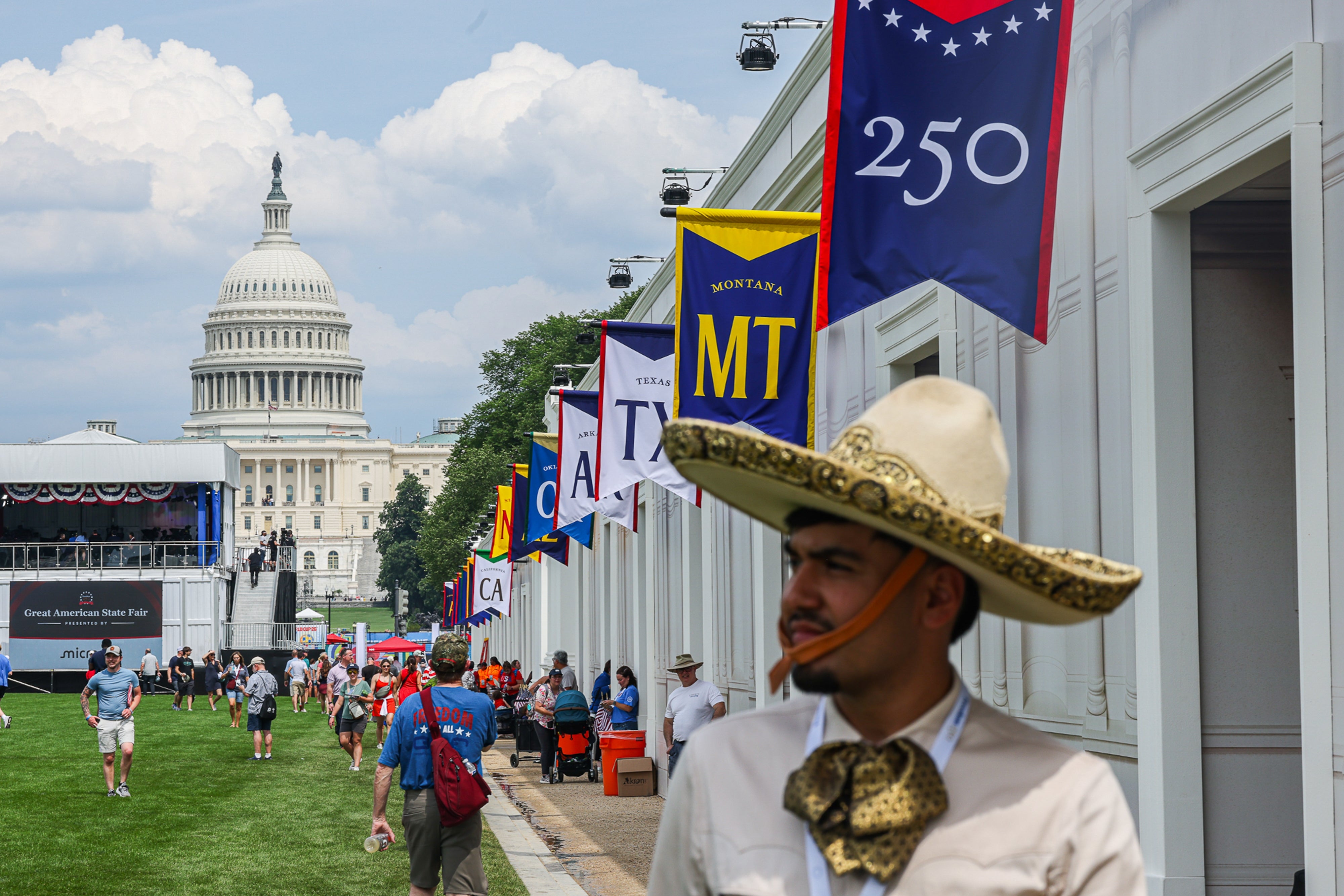 Seorang pria bertopi besar berdiri di depan US Capitol, dengan bendera negara berjajar di jalan selama acara publik