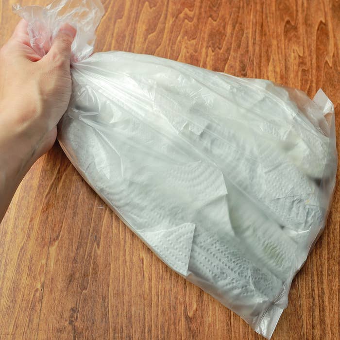 ビニール袋を手で持ち、木製のテーブルに置かれている。内部には何かが詰まっている様子。
