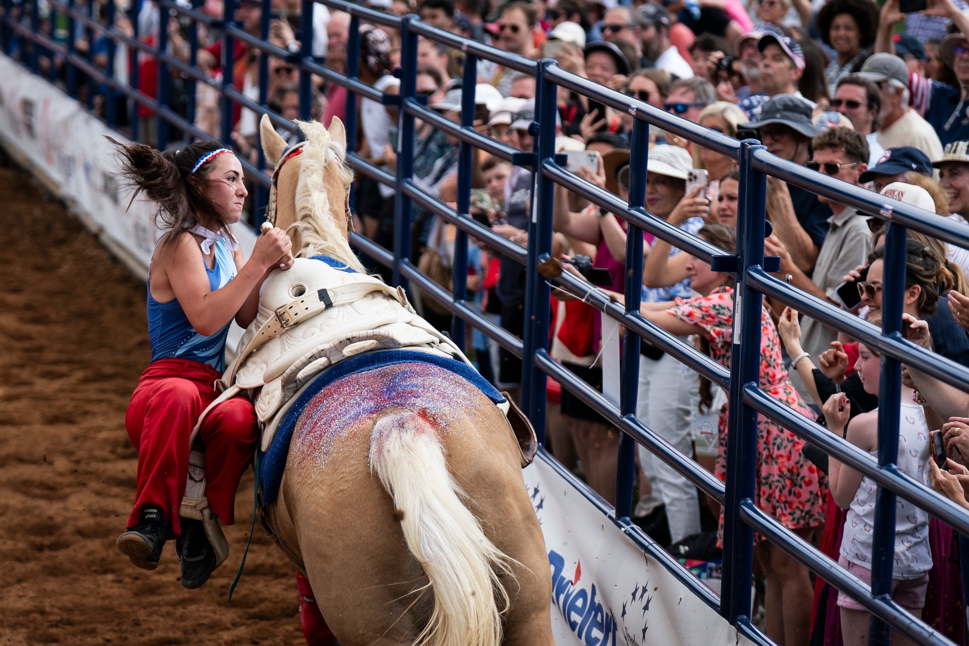 Person i rodeo-antrekk rir på en hest i en arena, omgitt av jublende folkemengder bak et gjerde