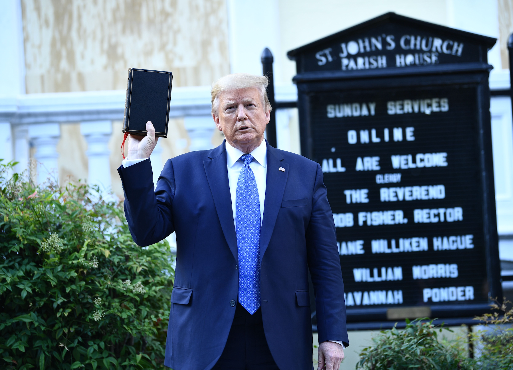 Donald Trump holder en bok foran et kirkeskilt med nettgudstjenester på søndager og navn på prester