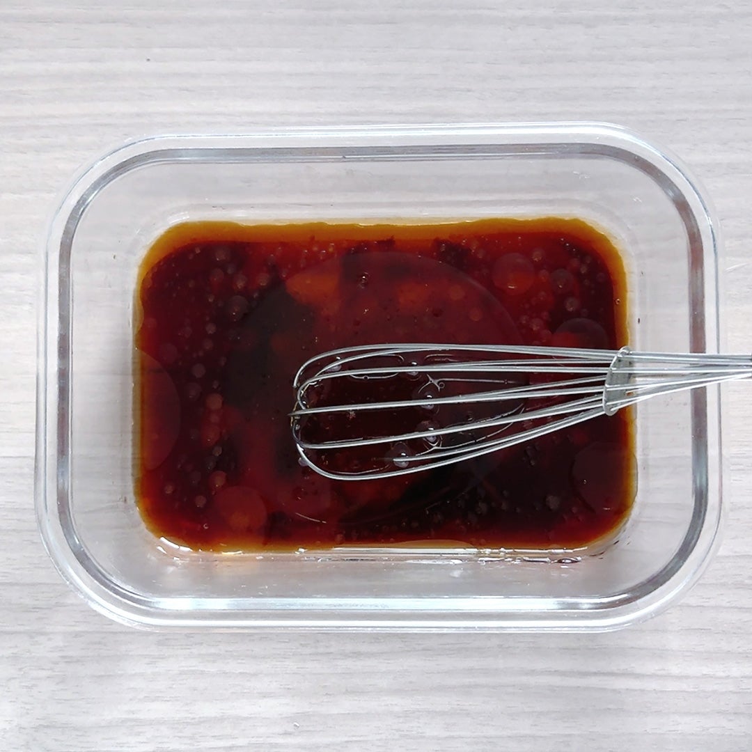 透明な容器に入った液体調味料を泡だて器で混ぜている様子。