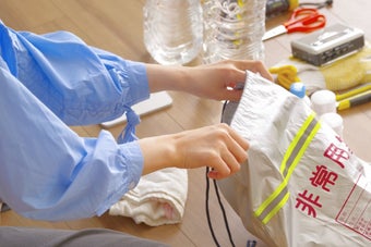 災害用バッグに物品を詰めている人。周囲に水や手袋などの防災用品が並んでいる。