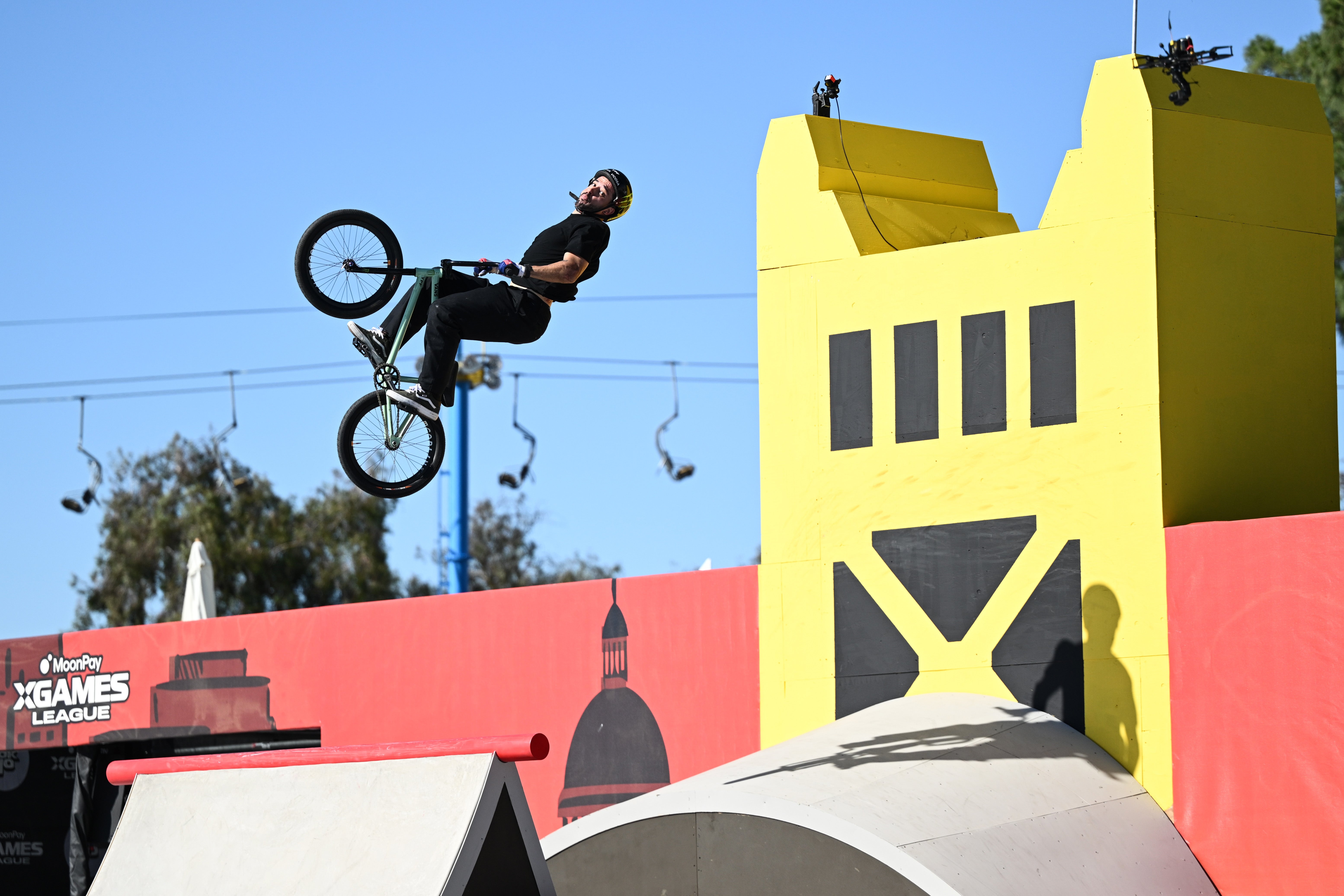 BMX rider performing a mid-air instrumentality   adjacent   agleam  yellowish  ramps with surrounding spectators and lawsuit   banners