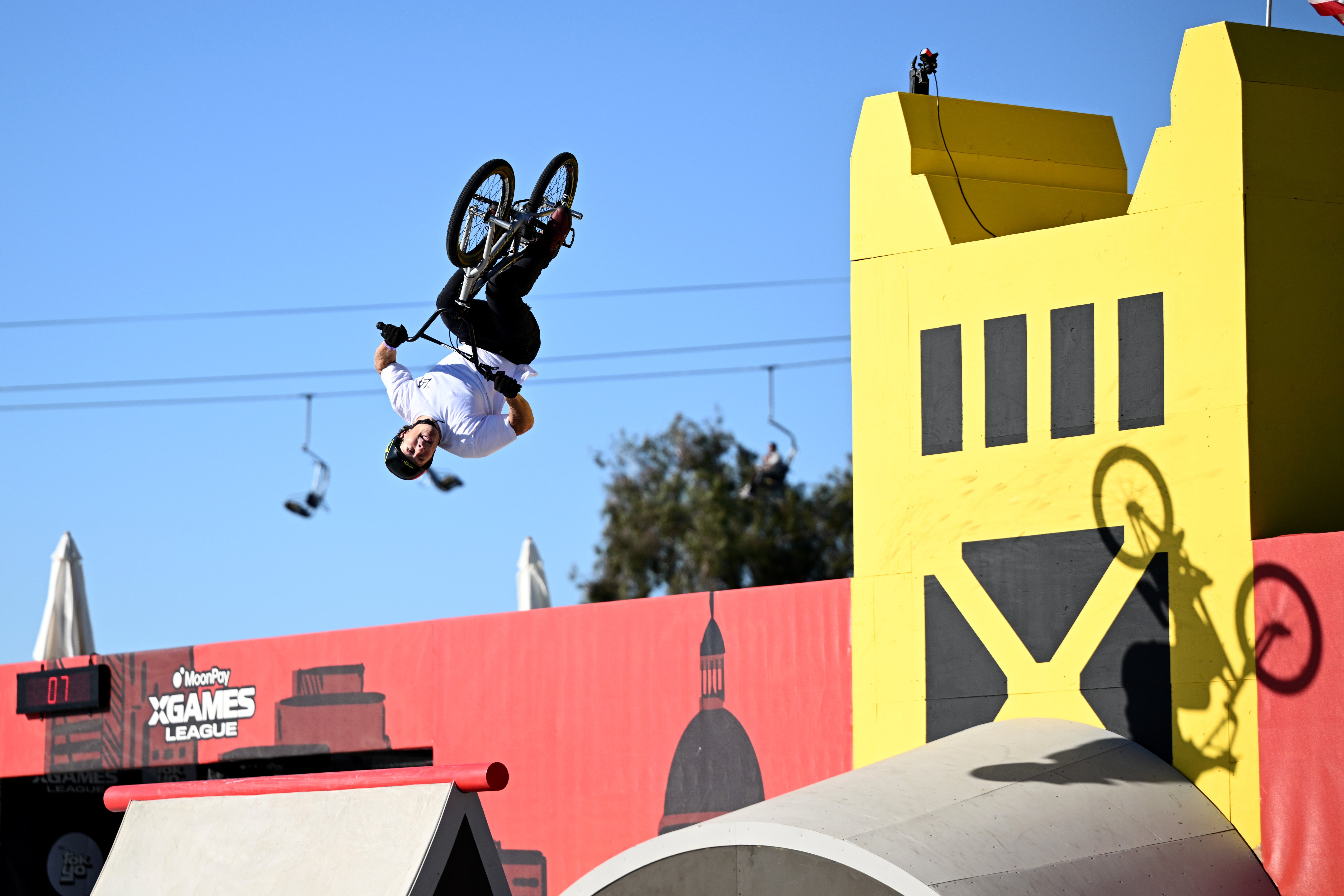 BMX rider performs a backflip during a stunt astatine  X Games League event, with ramps and a yellowish  operation   successful  the background