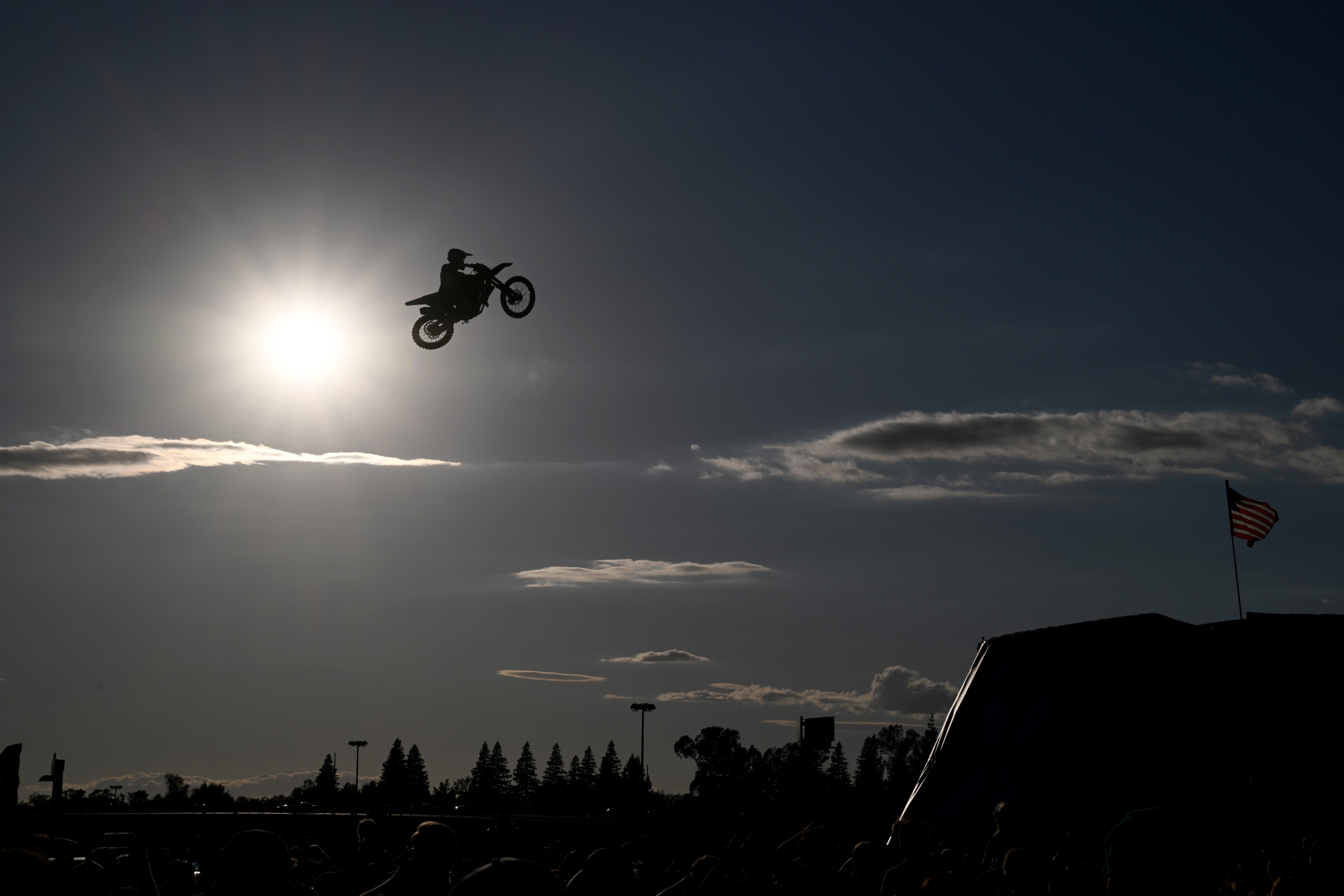 Silhouetted motorcyclist performing a precocious   leap  against a sunset sky, with trees and an American emblem  successful  the background
