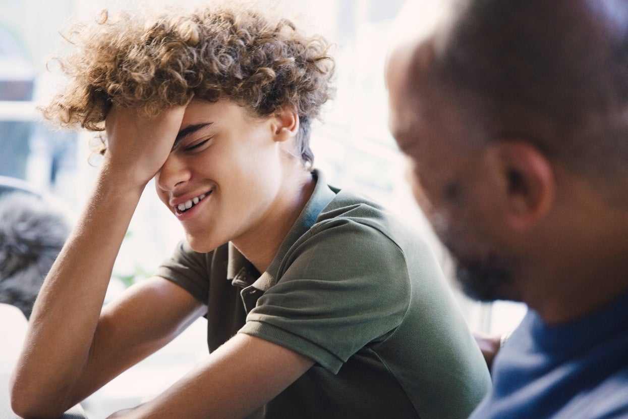 Teen smiling with hand on face, engaging in a joyful conversation with an adult. Warm interaction in a casual setting