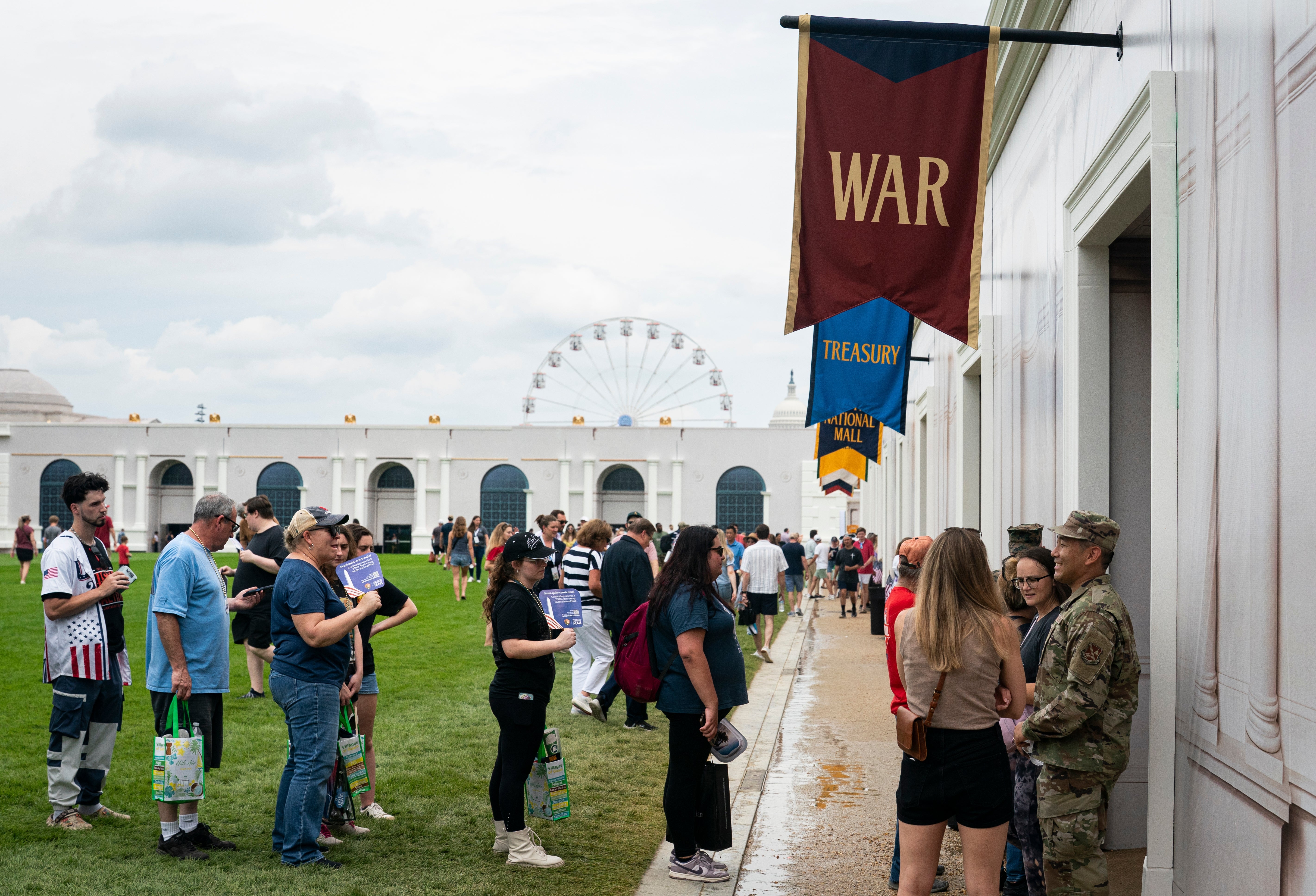 People waiting successful enactment astatine a themed lawsuit with banners marked "War" and "Treasury." A Ferris instrumentality is disposable successful the background