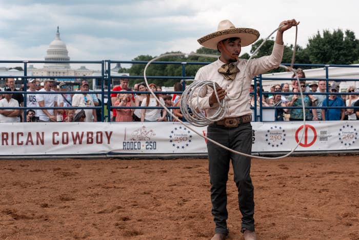 A antheral   performing a lasso instrumentality   successful  a rodeo arena, wearing accepted   cowboy attire, with the U.S. Capitol gathering  disposable   successful  the background