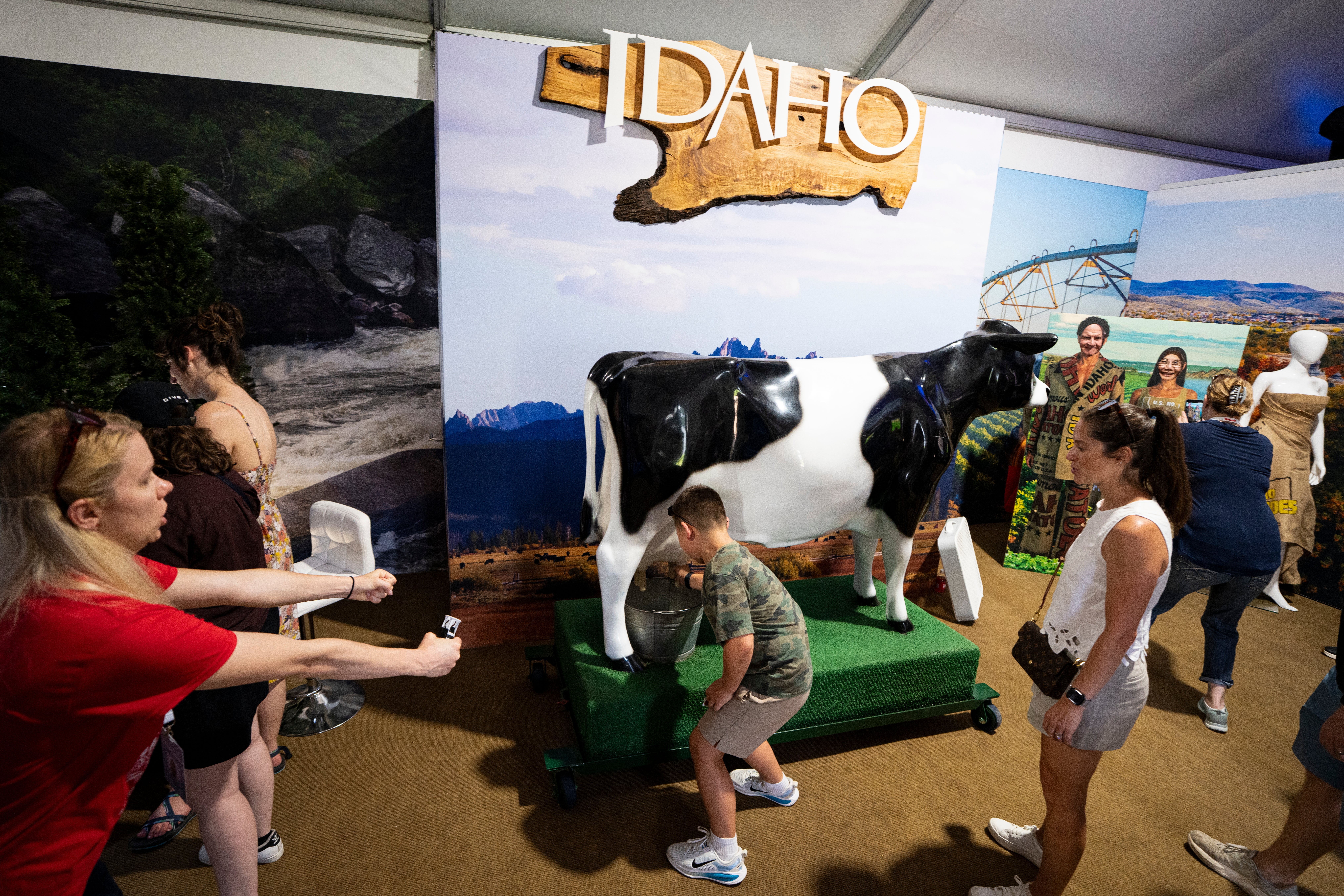 People interact with a cattle sculpture astatine the Idaho grounds successful an lawsuit space. A ample "Idaho" motion is displayed above