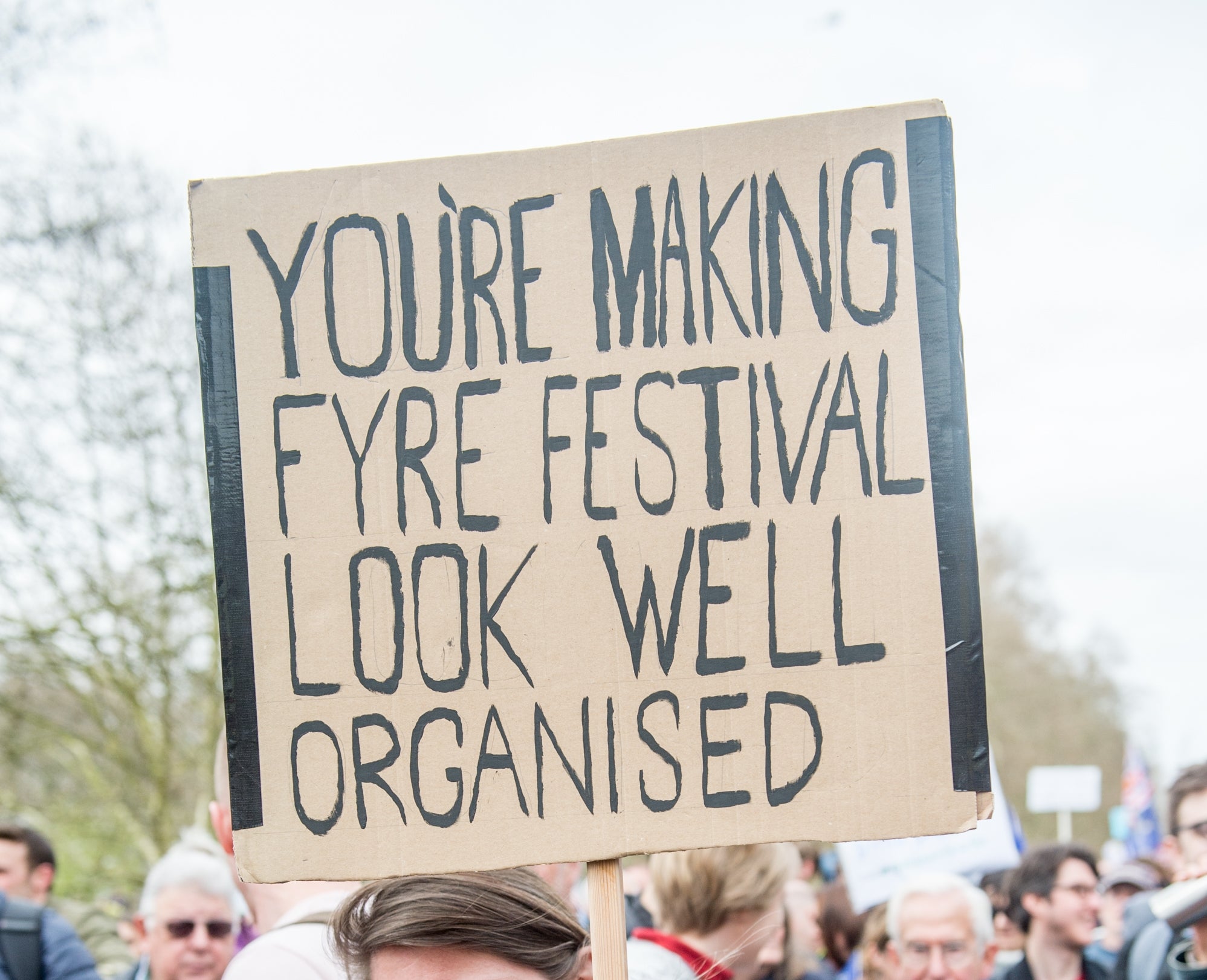 Person successful a assemblage holding a motion saying, "You're making Fyre Festival look good organized," smiling astatine a nationalist demonstration