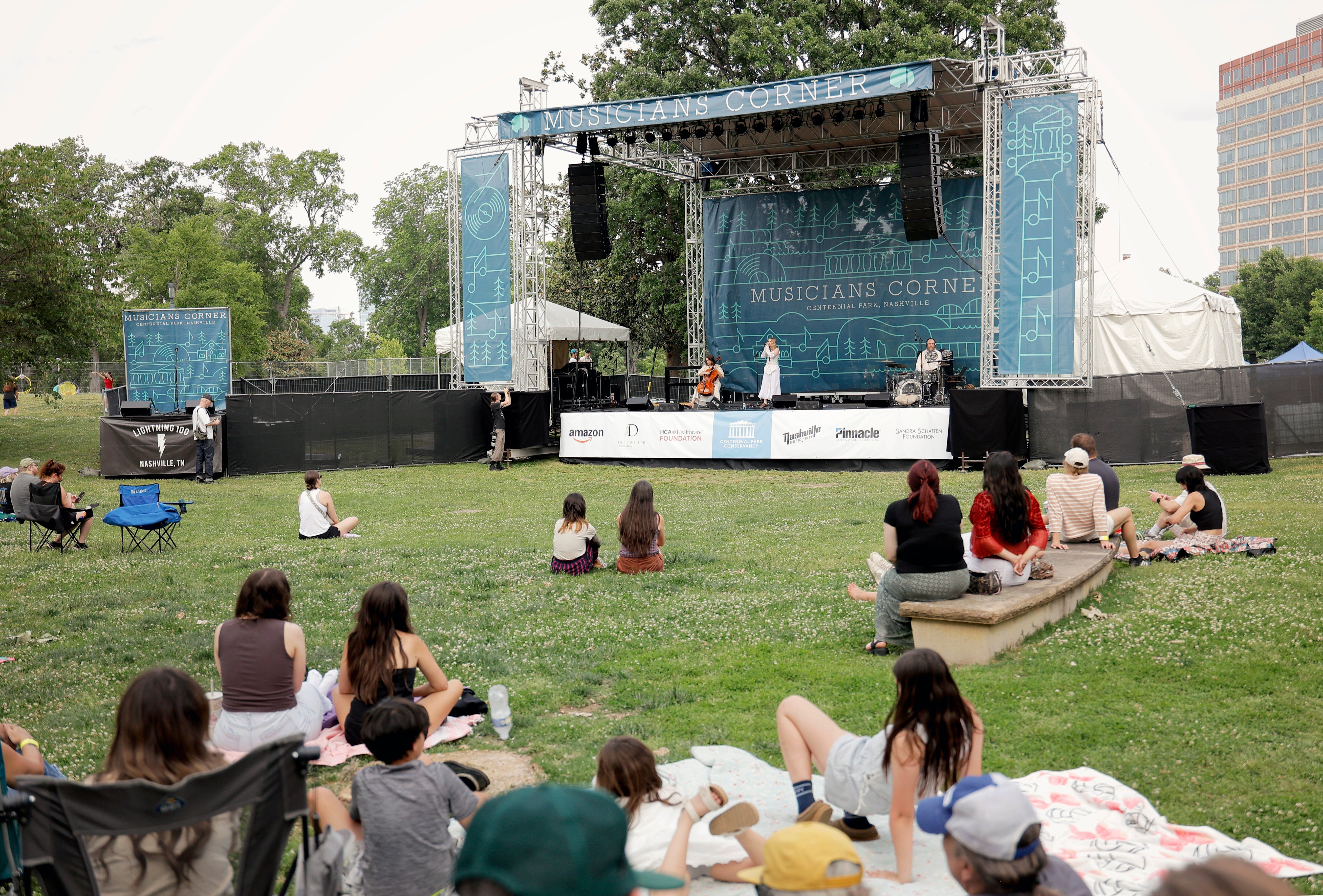 People sitting connected writer astatine an outdoor performance watching performers connected a signifier labeled "Musicians Corner."