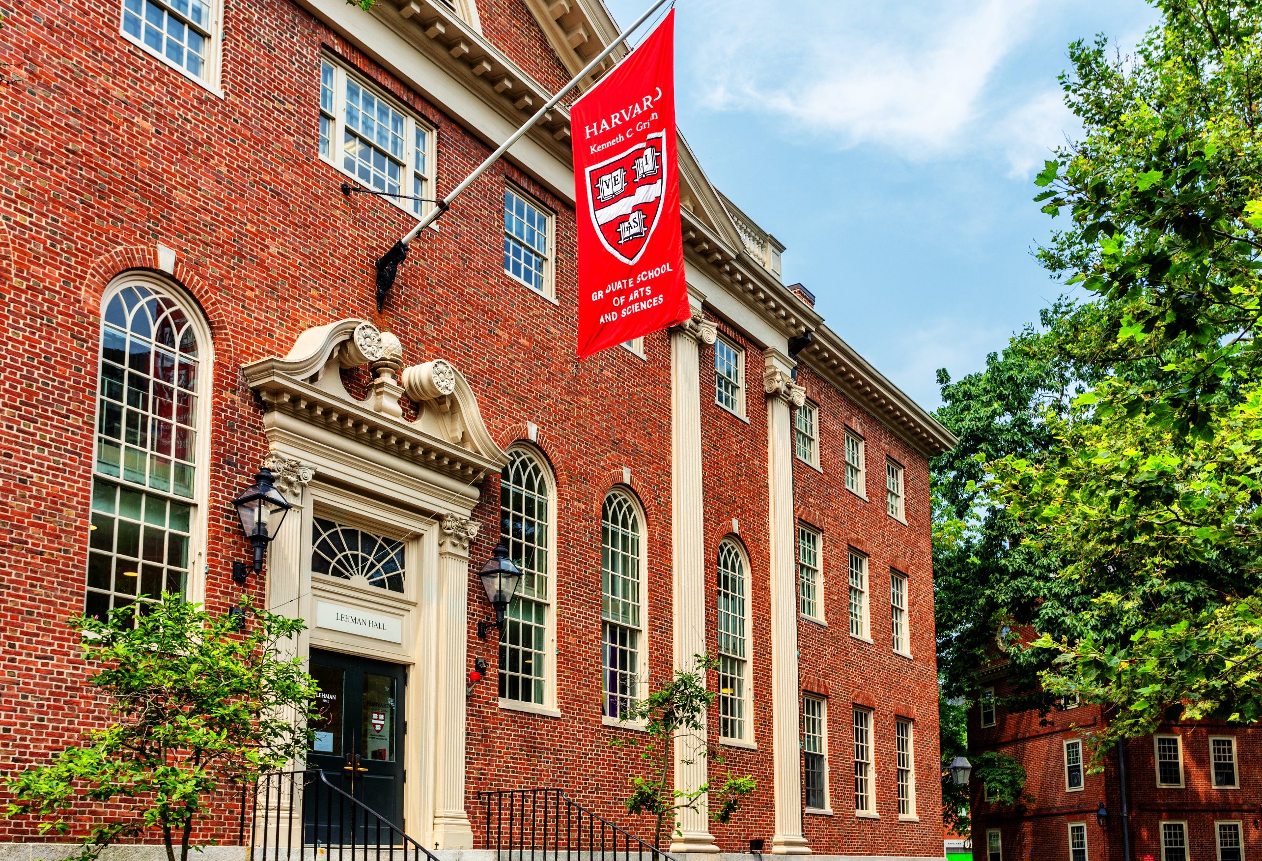 Historic ceramic gathering with arched windows and a Harvard banner. Lush greenish trees framework the country connected a wide day