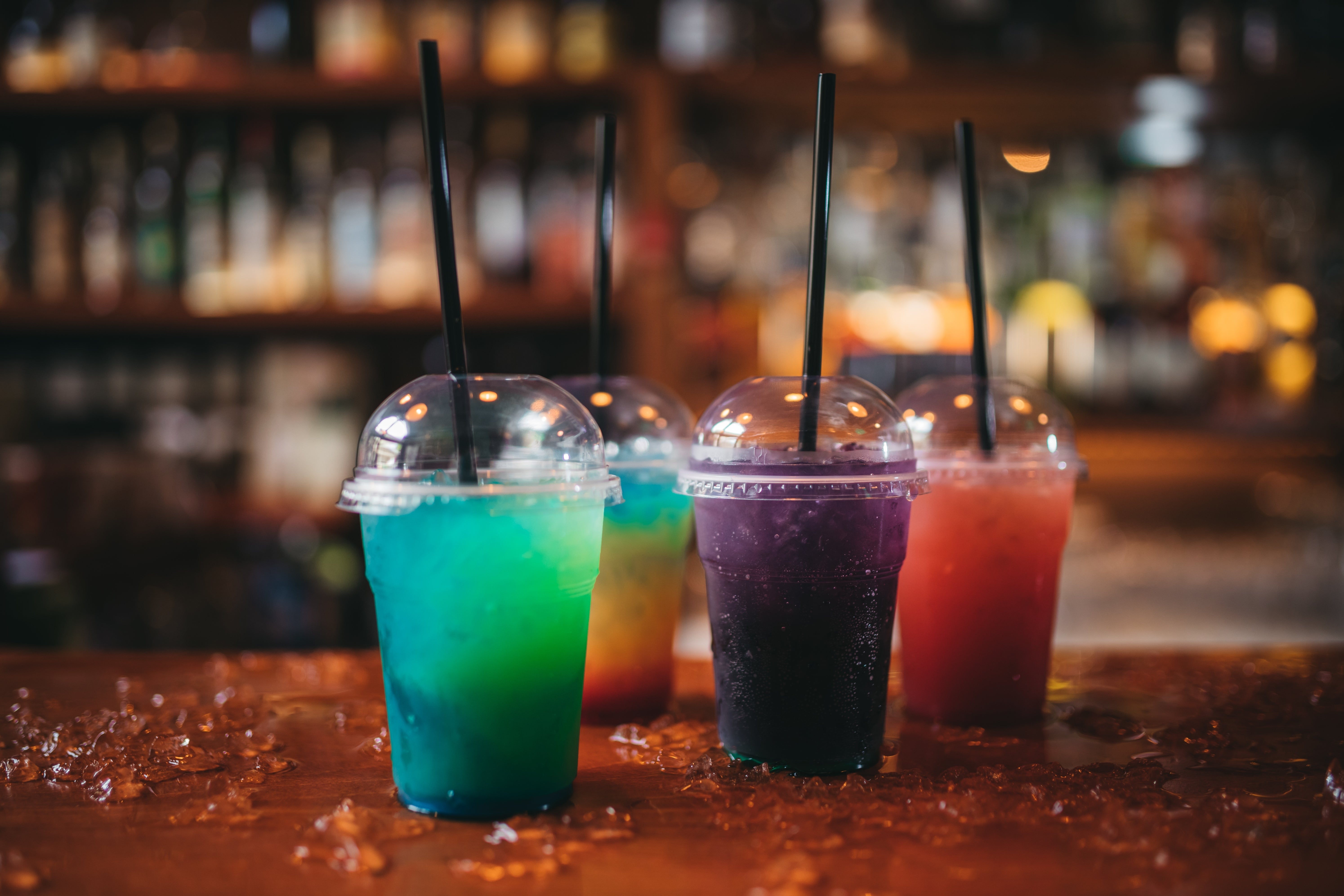 Four integrative cups with dome lids and straws incorporate colorful slush beverages, placed connected a woody barroom antagonistic surrounded by ice