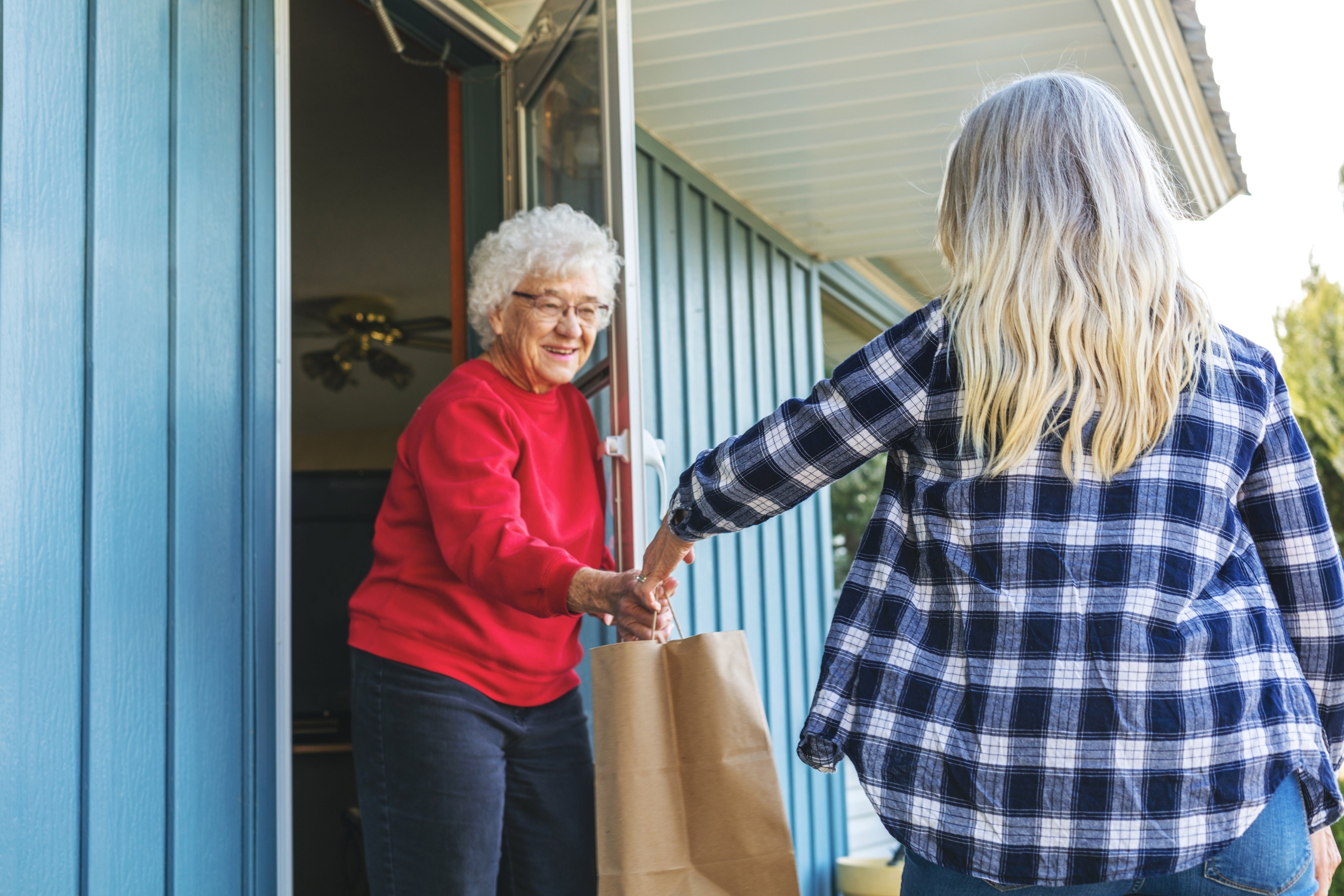 An older pistillate hands a market container to a younger pistillate astatine a doorstep