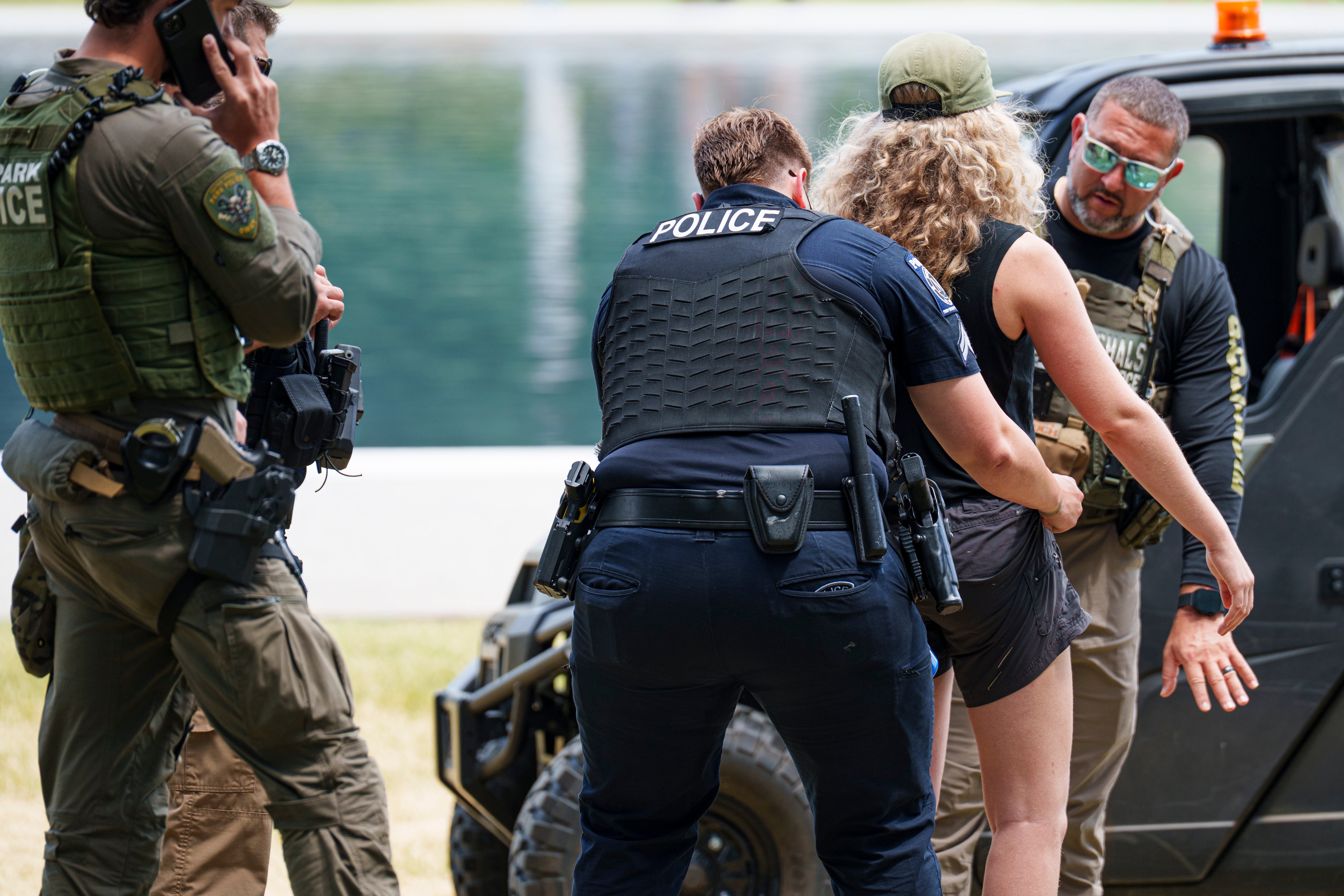 Law enforcement officers apprehension  a idiosyncratic   adjacent   a vehicle, with a water  successful  the background