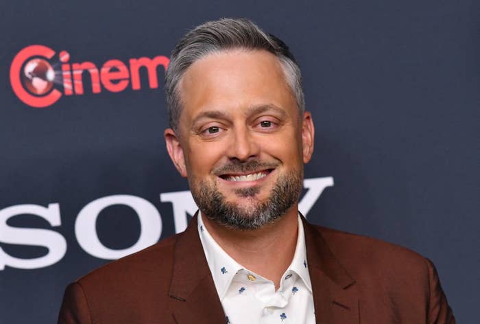 Man connected  reddish  carpet successful  a suit   with a patterned shirt, smiling for the camera