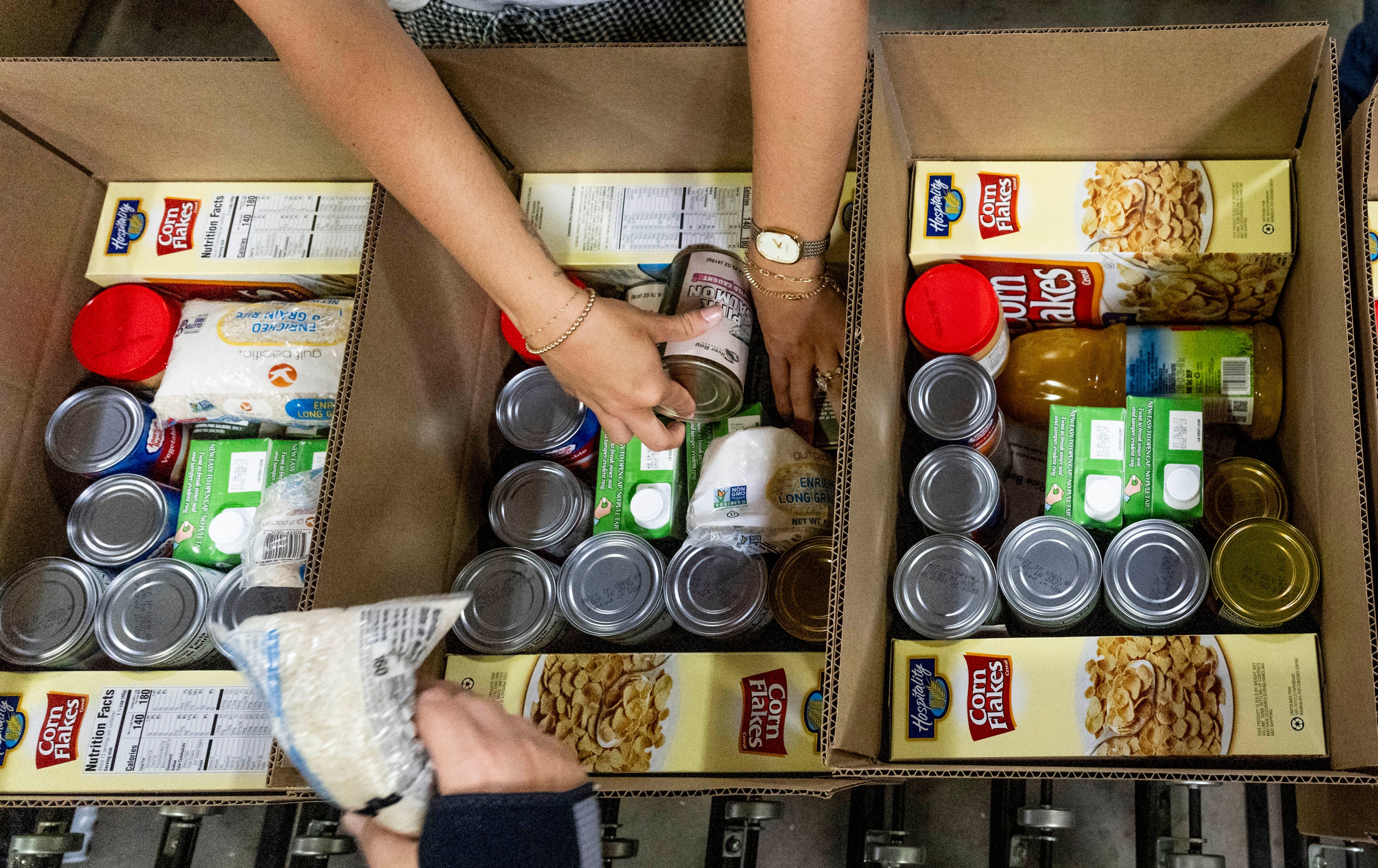 Hands packing canned food, cereal, pasta, and foodstuff into boxes, suggesting a nutrient donation oregon organisation effort