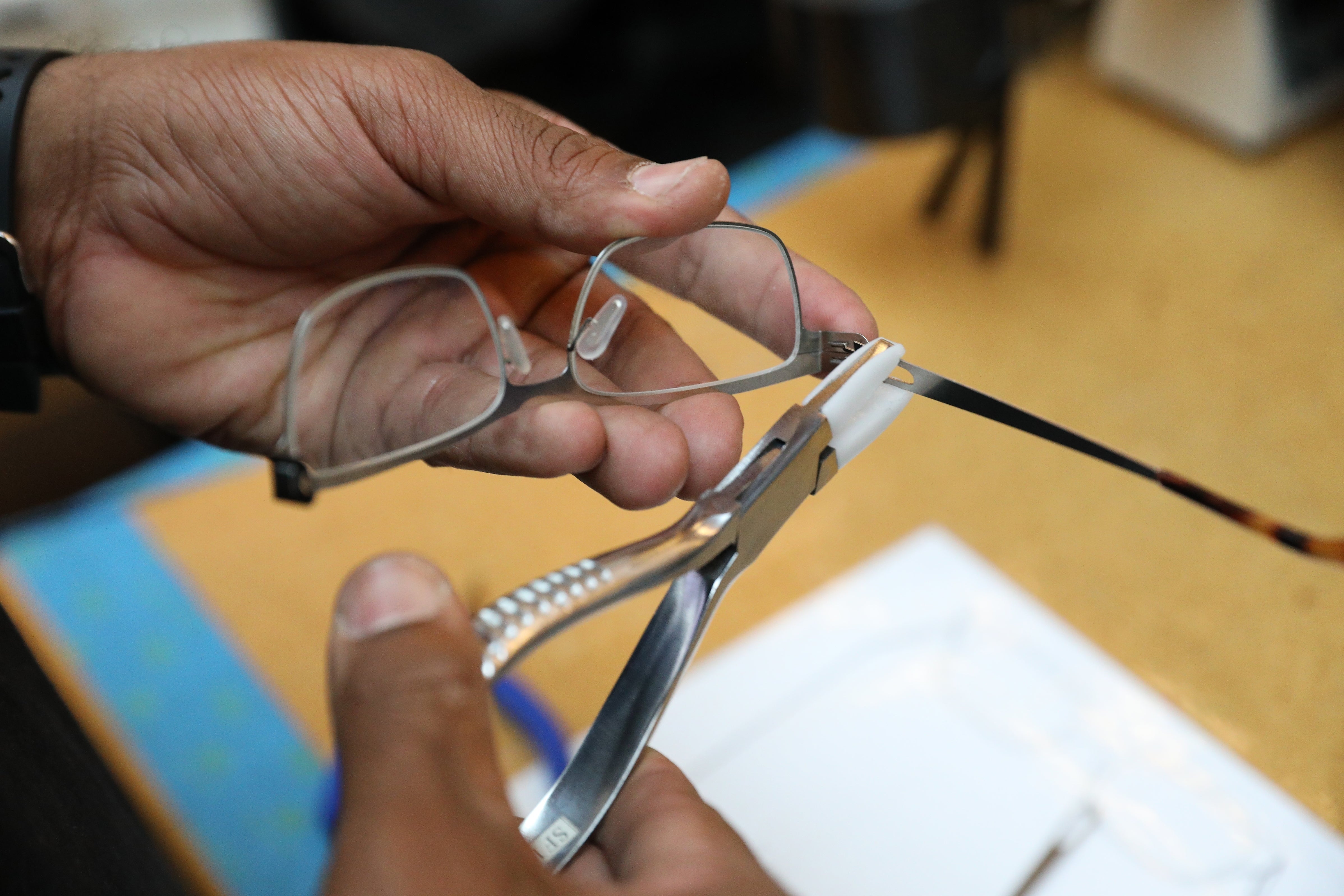 Hands adjusting eyeglass frames with pliers connected a workbench, suggesting repair oregon maintenance