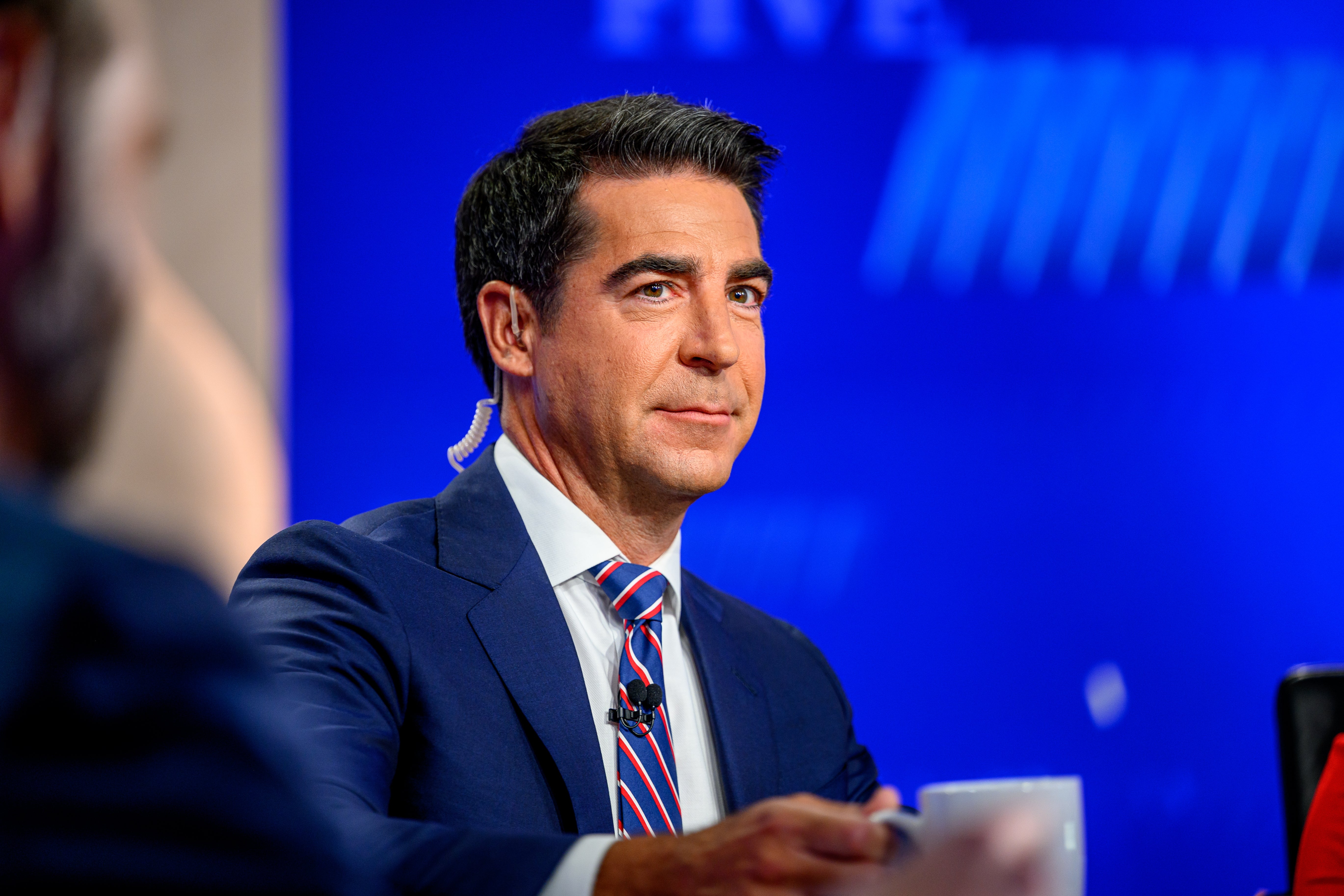 A idiosyncratic   successful  a suit   and necktie  appears connected  a quality    amusement   set, holding a achromatic  mug, with workplace  lighting and instrumentality  successful  the background