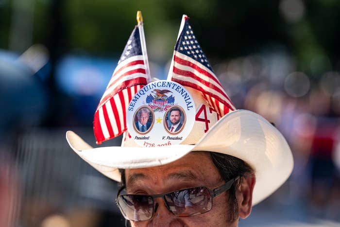 Man wearing a chapeau  with 2  tiny  U.S. flags and a fastener  displaying images of humanities  figures and "Semiquincentennial" text